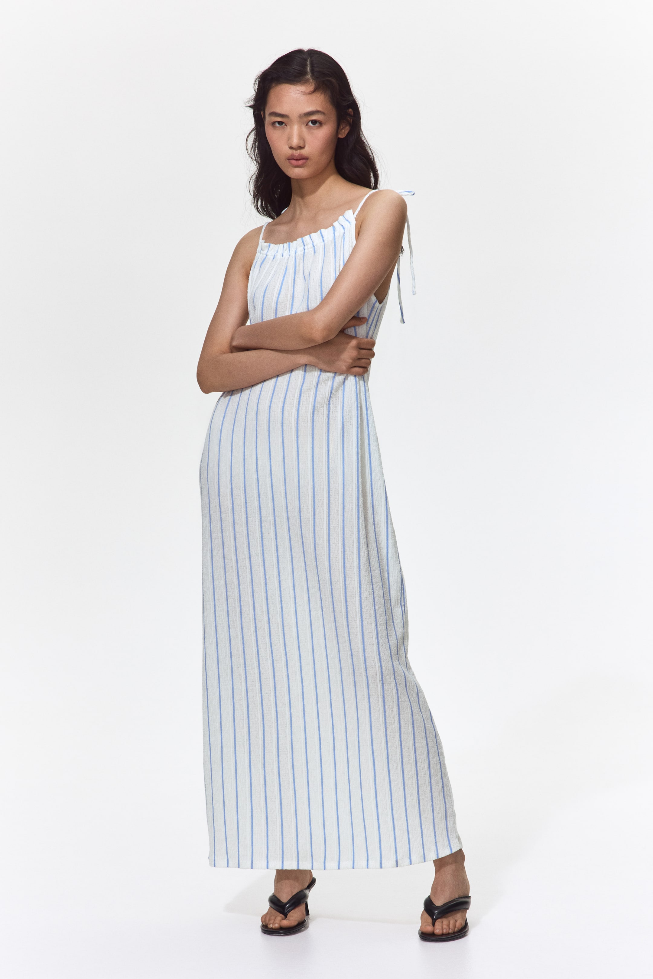 Voir une image plus grande: Une robe longue et ample en jersey blanc froissé avec des rayures verticales bleues est portée par le mannequin. La robe présente un décolleté orné de volants, et des bretelles étroites à nouer passent par l'encolure.