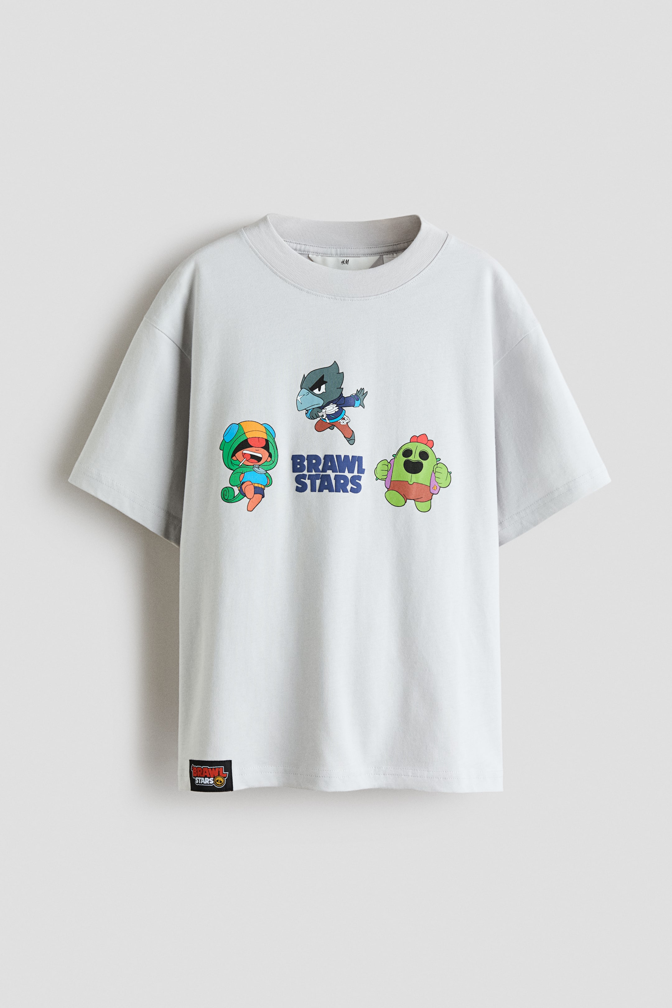 View larger image: A light gray T-shirt is shown from the front, offering a relaxed fit with dropped shoulders and a ribbed trim around the crew neckline. It features a graphic print on the front, displaying three colorful cartoon characters and the words 'BRAWL STARS,' with a small black logo tag visible on the bottom left hem.