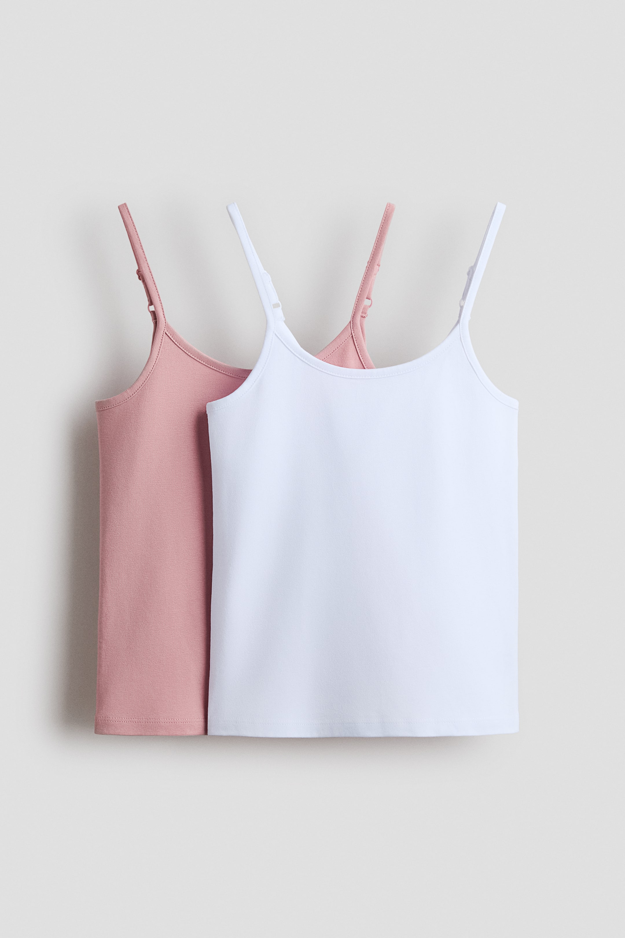 Grotere afbeelding bekijken: Tops van zacht katoenjersey worden getoond, waarbij een witte top voor een rozekleurige top is geplaatst. Beide tops hebben verstelbare spaghettibandjes en een rechte zoom.