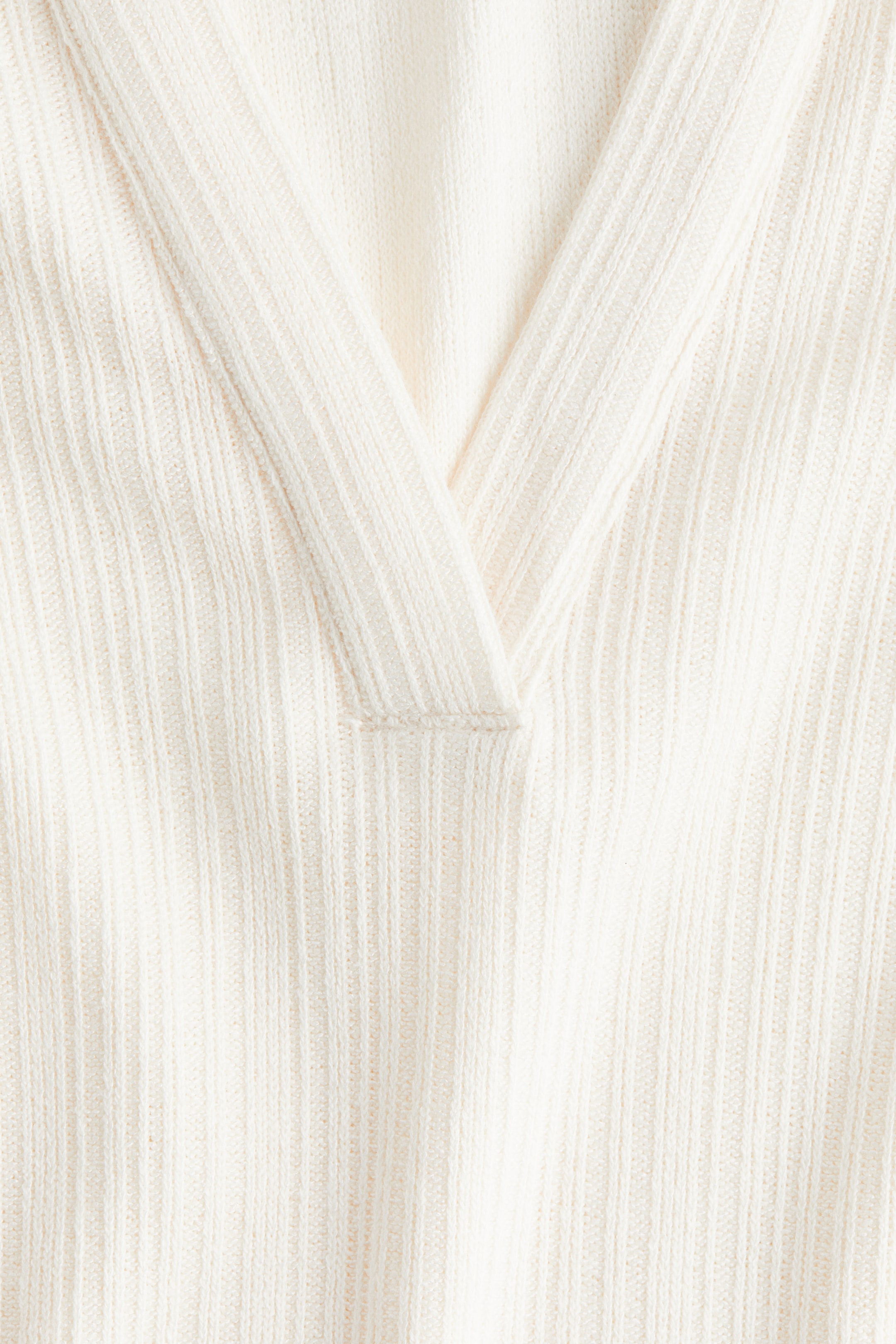 Xem ảnh lớn hơn: Một chiếc áo len dệt kim màu kem, có gân đang hiển thị cổ chữ V từ phía trước. Vải có kết cấu đang tạo thành phần mở cổ chữ V, với một chi tiết khâu ngang nhỏ ở đáy.