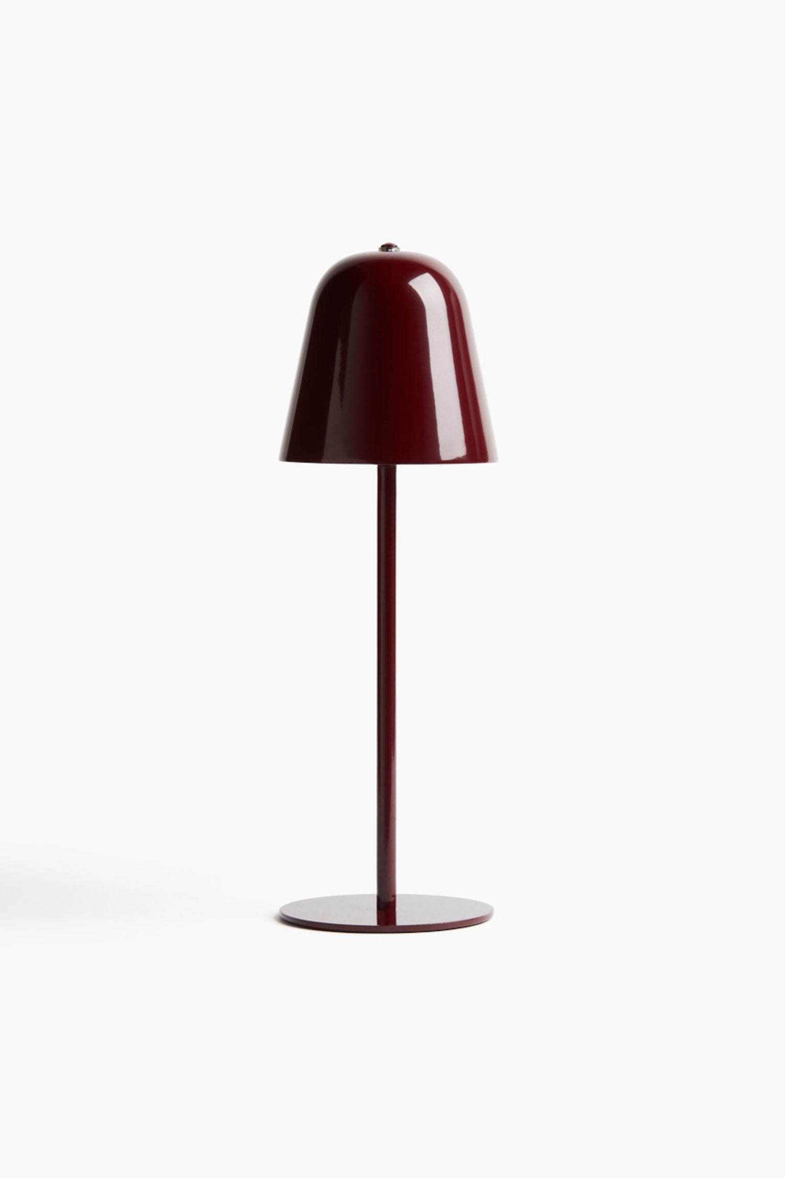 Eine bordeauxrote Tischlampe steht aufrecht und zeigt nach vorne. Sie präsentiert einen glänzenden, kuppelförmigen Schirm, der von einem schlanken zylindrischen Stiel und einem flachen, runden Fuß getragen wird.