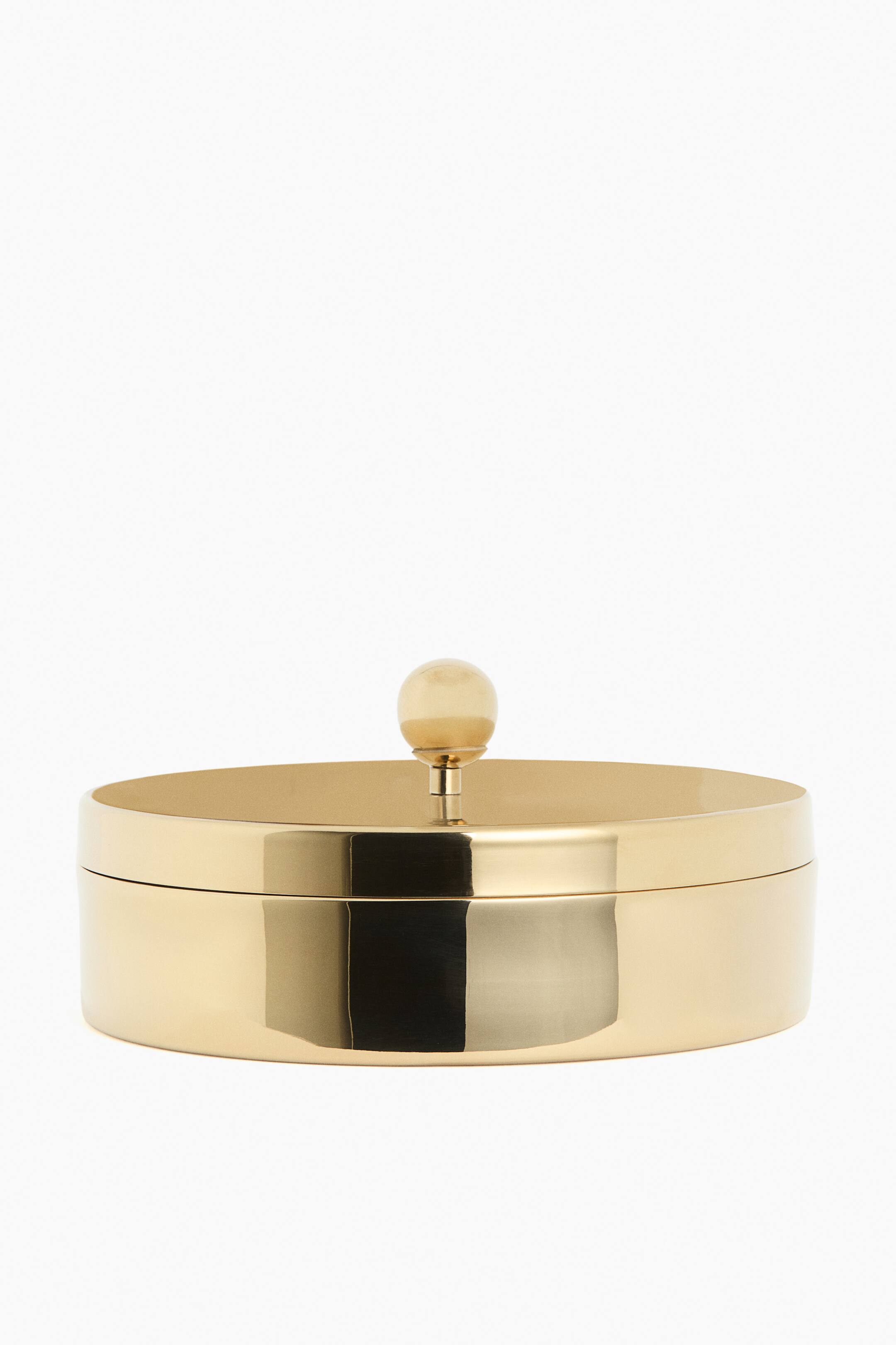 View larger image: A circular box is reflecting light with its polished gold-toned metal surface. It features a flat lid topped with a spherical knob.