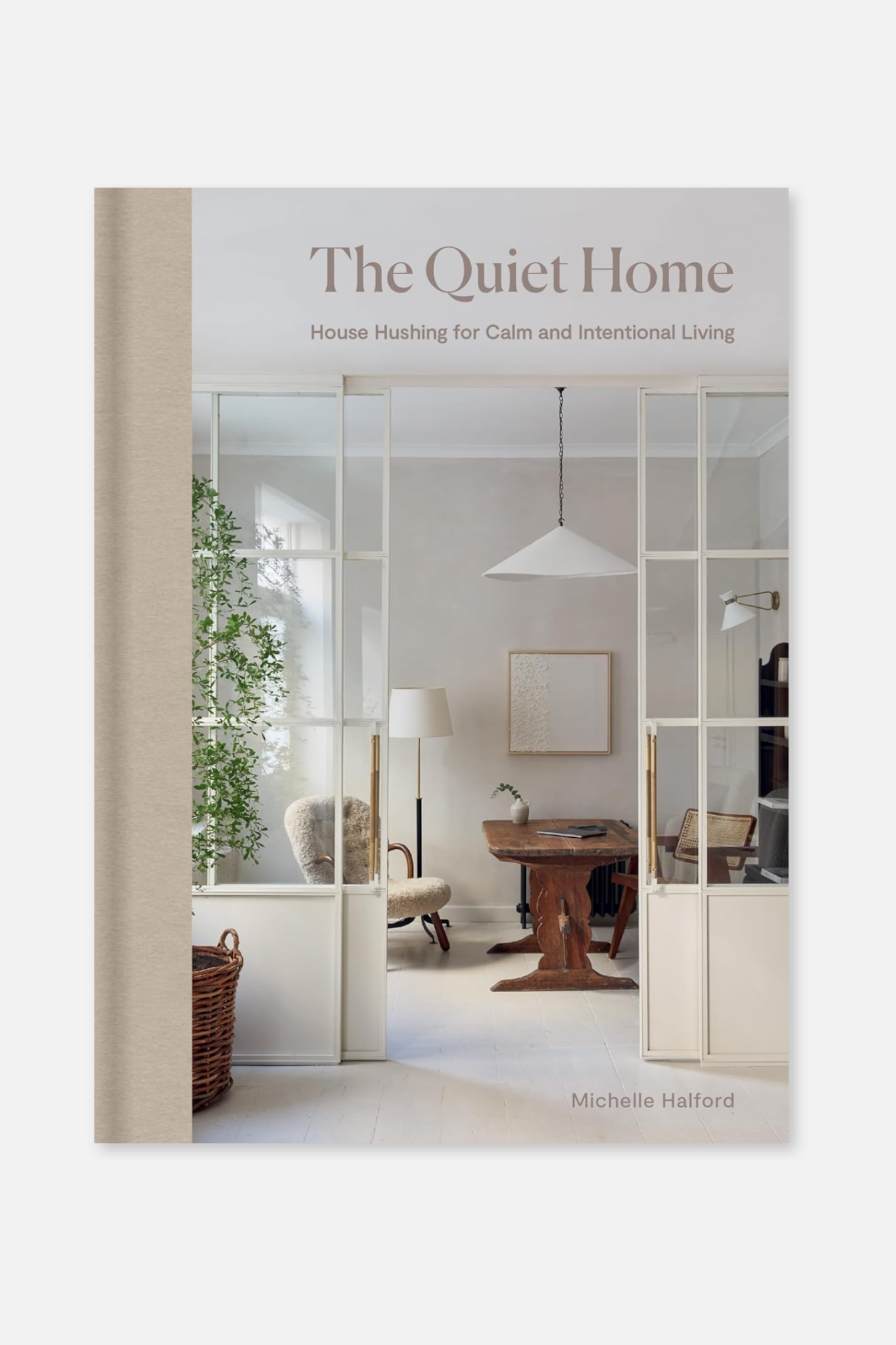 Größeres Bild anzeigen: Das Buchcover von "The Quiet Home" zeigt einen Innenraum mit einem Holztisch, Stühlen und einer Pflanze, während ein vertikaler beiger Texturstreifen entlang des linken Randes verläuft. Der Titel "The Quiet Home", der Untertitel "House Hushing for Calm and Intentional Living" und die Autorin "Michelle Halford" erscheinen in brauner Serifenschrift.