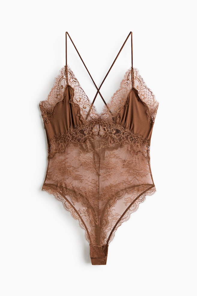 A brown satin and lace bodysuit featuring a deep V-neckline with scalloped lace trim and slender criss-cross back straps. The body is designed with sheer floral lace panelling and scalloped edges, extending to a thong-style bottom with a snap closure. - 1