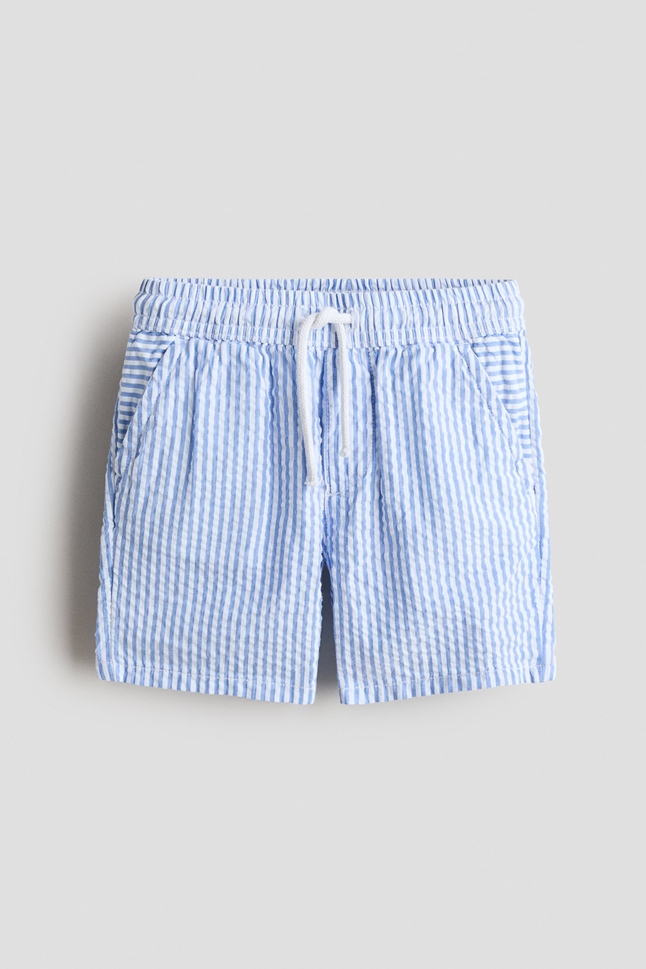 Grösseres Bild ansehen: Shorts präsentieren FRONT, mit einem blau-weiß gestreiften Seersucker-Muster. Sie sind mit einem elastischen Bund gestaltet, durch den eine weiße Kordel gezogen ist, und zwei Seitentaschen sind sichtbar.