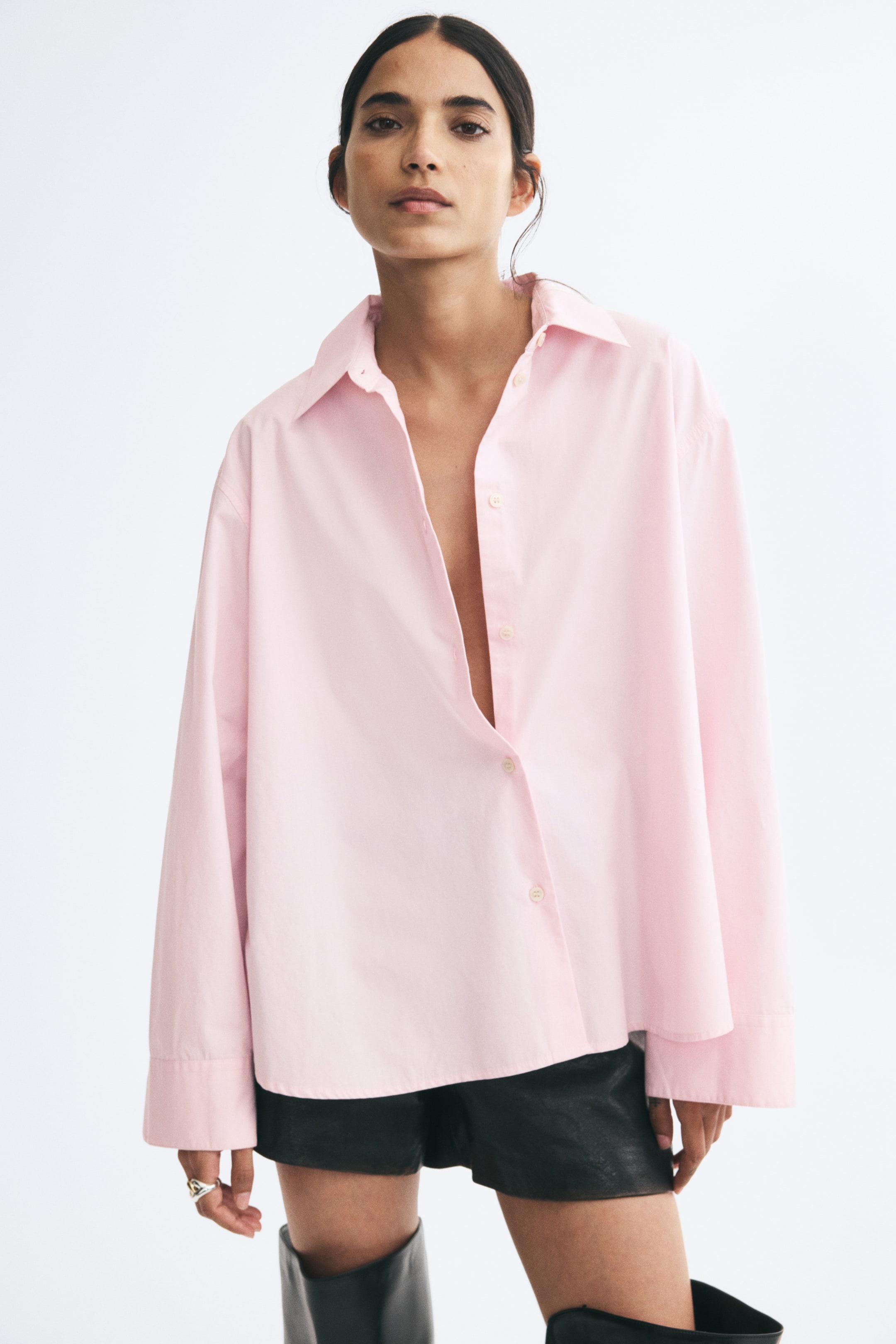View larger image: A light pink, relaxed-fit shirt in a cotton weave is being worn by the model. The shirt features a pointed collar, dropped shoulders, long sleeves with button cuffs, and a partially open button-down front.