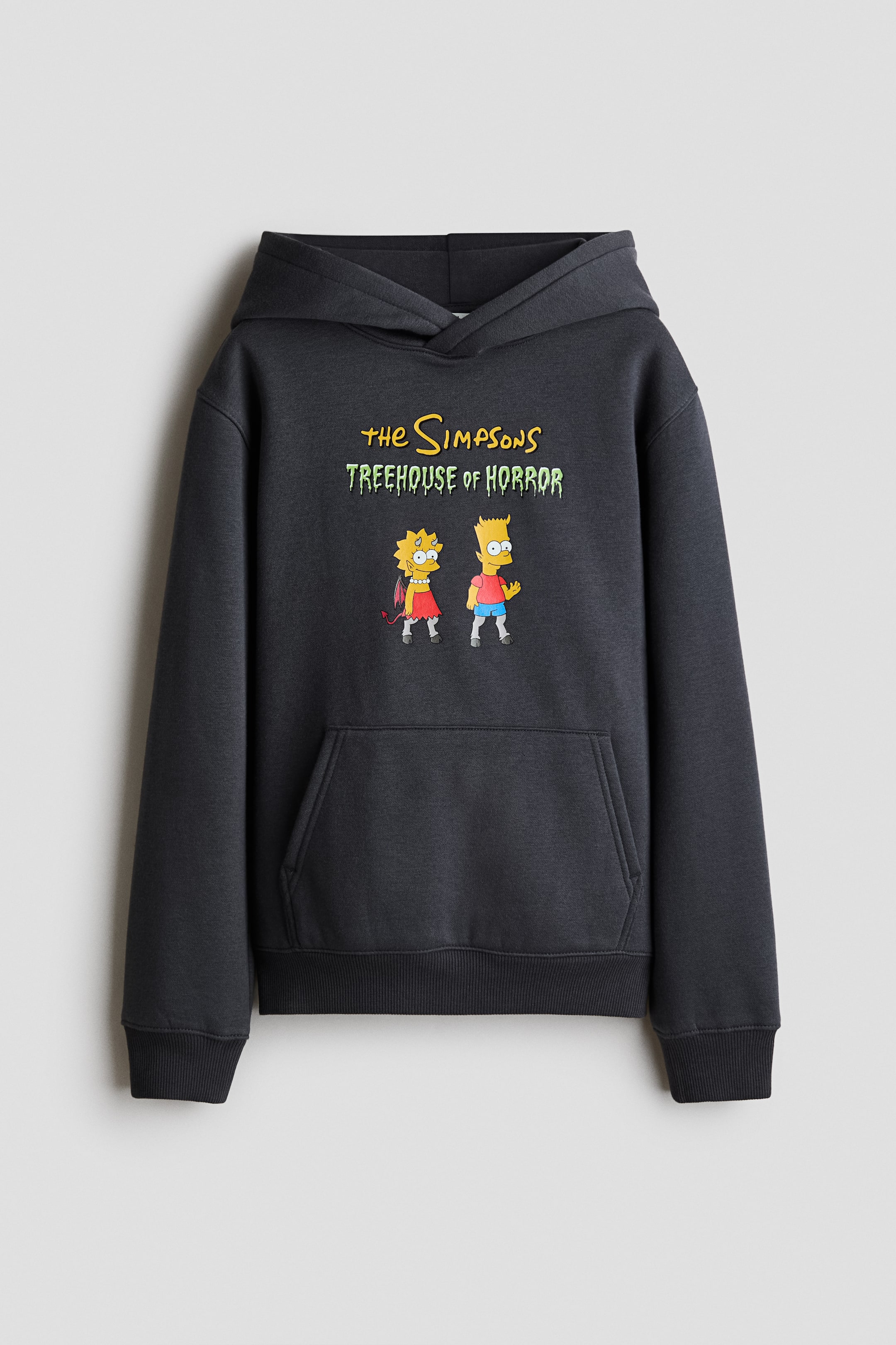 View larger image: A dark grey hoodie is shown from the front, featuring a hood, ribbed cuffs, and a ribbed hem. The front displays ‘The Simpsons Treehouse of Horror’ text in yellow and green, with cartoon images of Lisa as a devil and Bart as a zombie.
