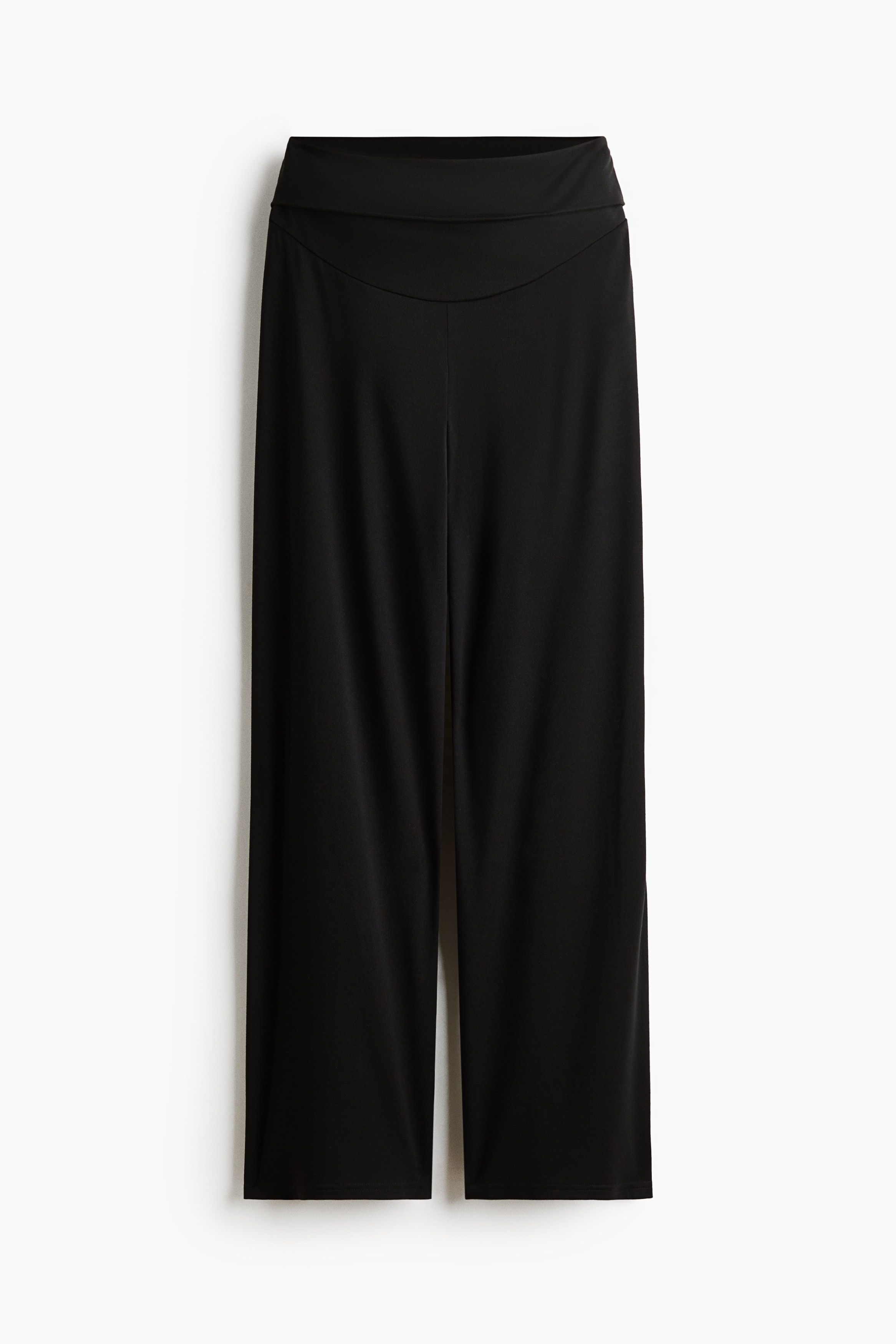 Crne Å¡iroke joga pantalone sa visokim, Å¡irokim pojasom koje model nosi tako da se pruÅ¾aju preko njenog trudniÄkog stomaka. Pantalone su stilizovane uz usklaÄen crni sportski grudnjak i crni dukser sa rajsferÅ¡lusom, prebaÄen preko ramena.