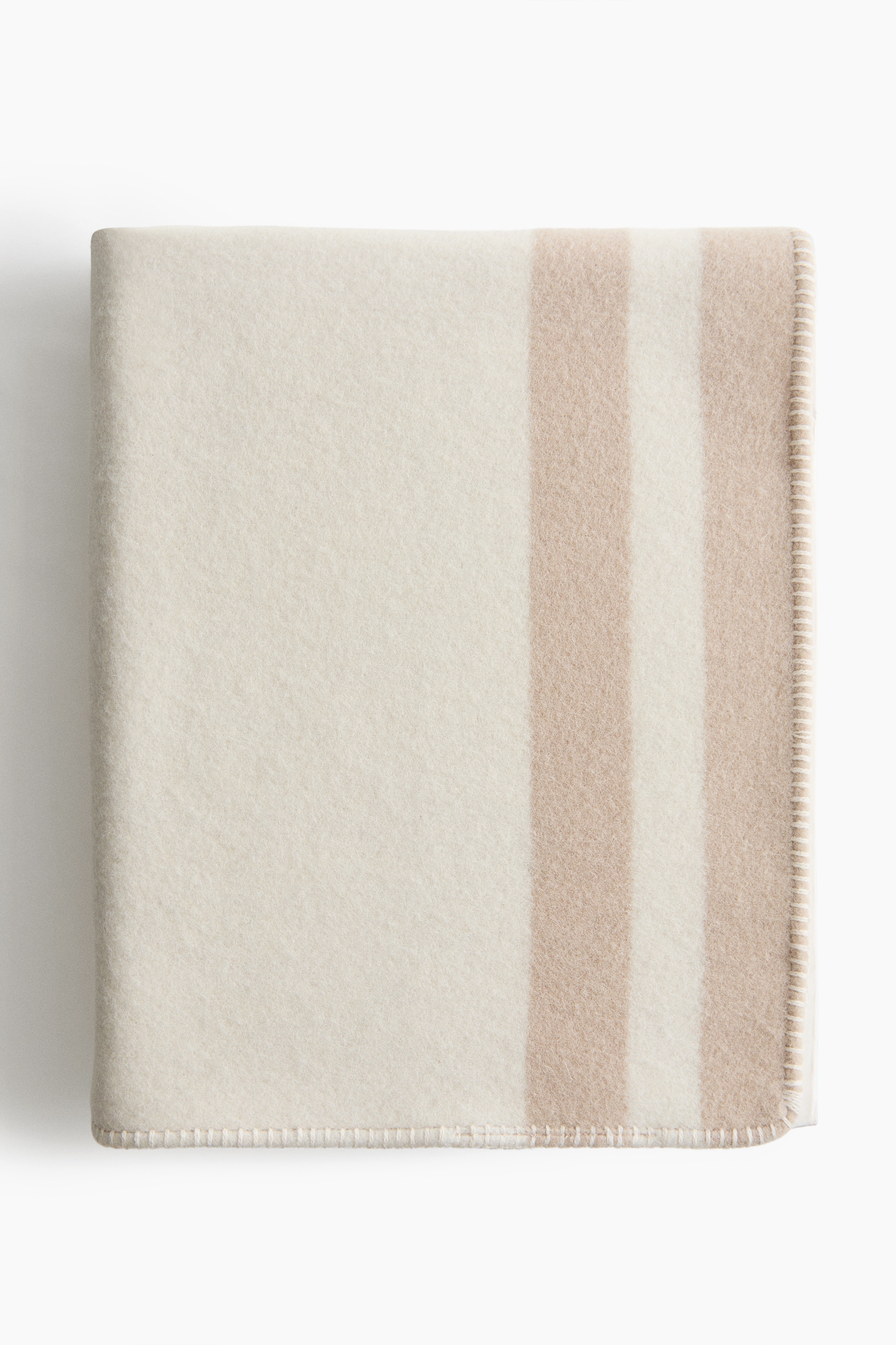 A soft wool-blend blanket is lying flat on a bed, showcasing a large beige printed design of a cartoon mouse face in the centre. The cream-coloured blanket features horizontal beige stripes near the top and neat blanket stitching along the edges.