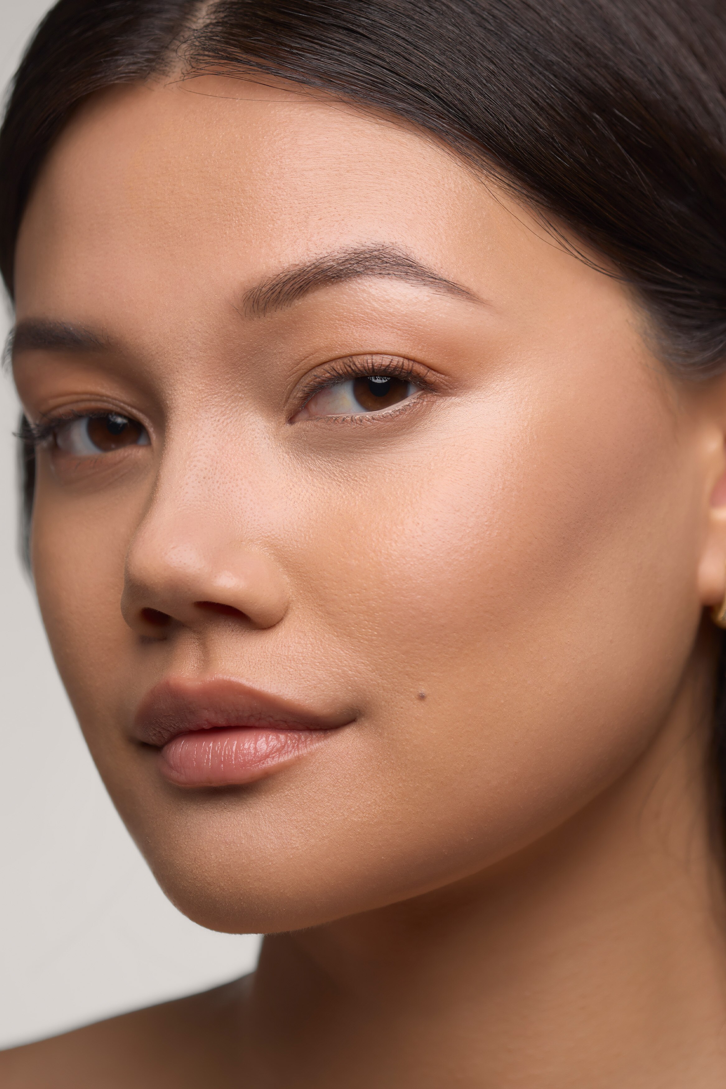 En hvit Morphe Shapelifter Micro Brightening Stick står vertikalt og viser en avrundet, lys ferskenfarget produktspiss på toppen. Den sylindriske hylsen har den grå «MORPHE»-logoen trykt vertikalt, med en matchende ferskenfarget kant som avslutter bunnen.