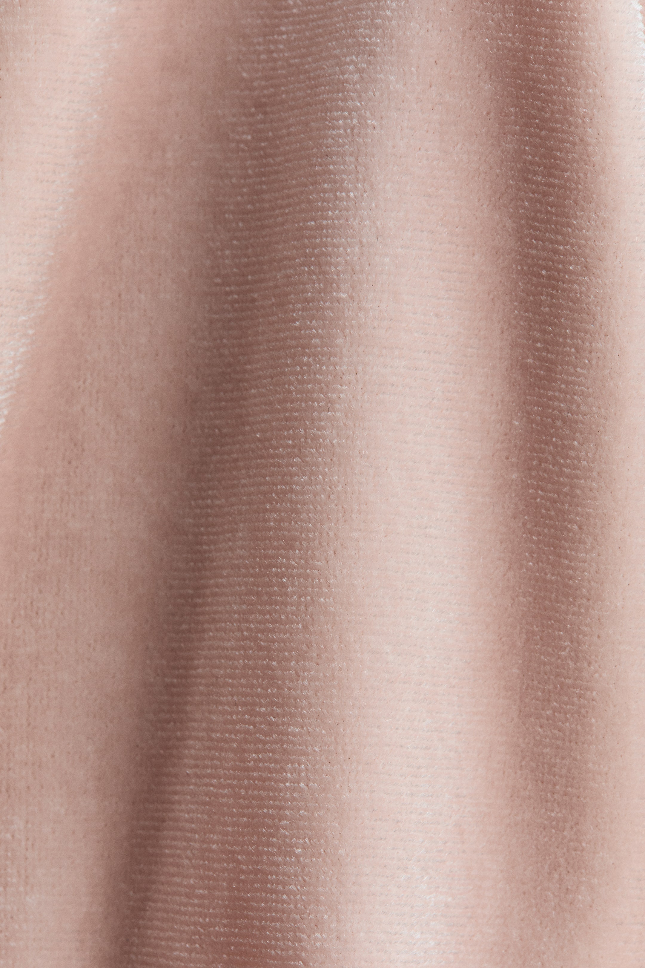 Agrandir l'image: Un tissu de couleur or rose clair présente une texture moelleuse, semblable au velours, avec un côtelage horizontal subtil. Le matériau est drapé en plis verticaux doux, créant des zones de lumière et d'ombre variées.