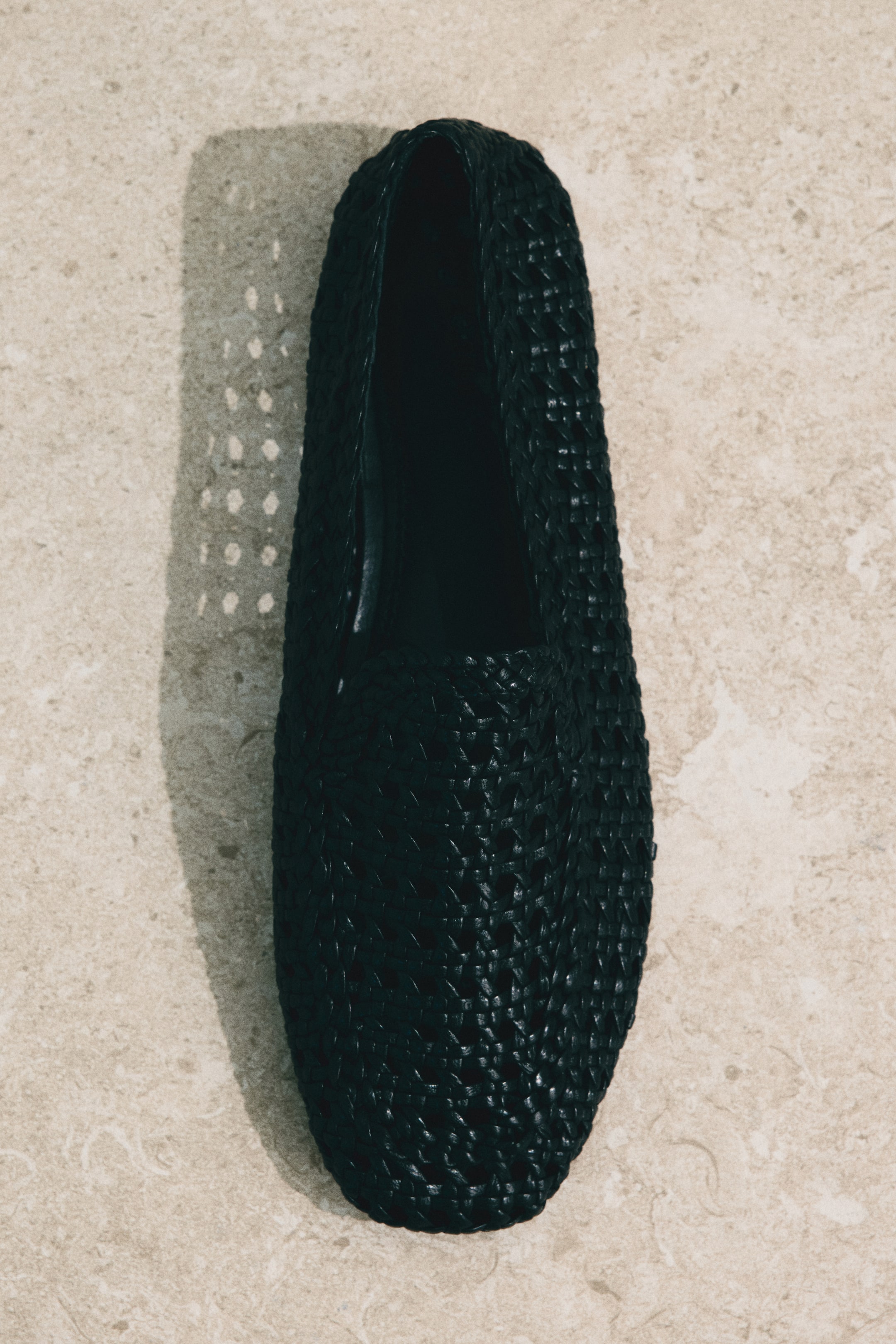 View larger image: A black slip-on loafer featuring a finely woven upper with an intricate, open pattern. Its dark interior is visible, and it is lying flat, viewed from a top-down perspective.