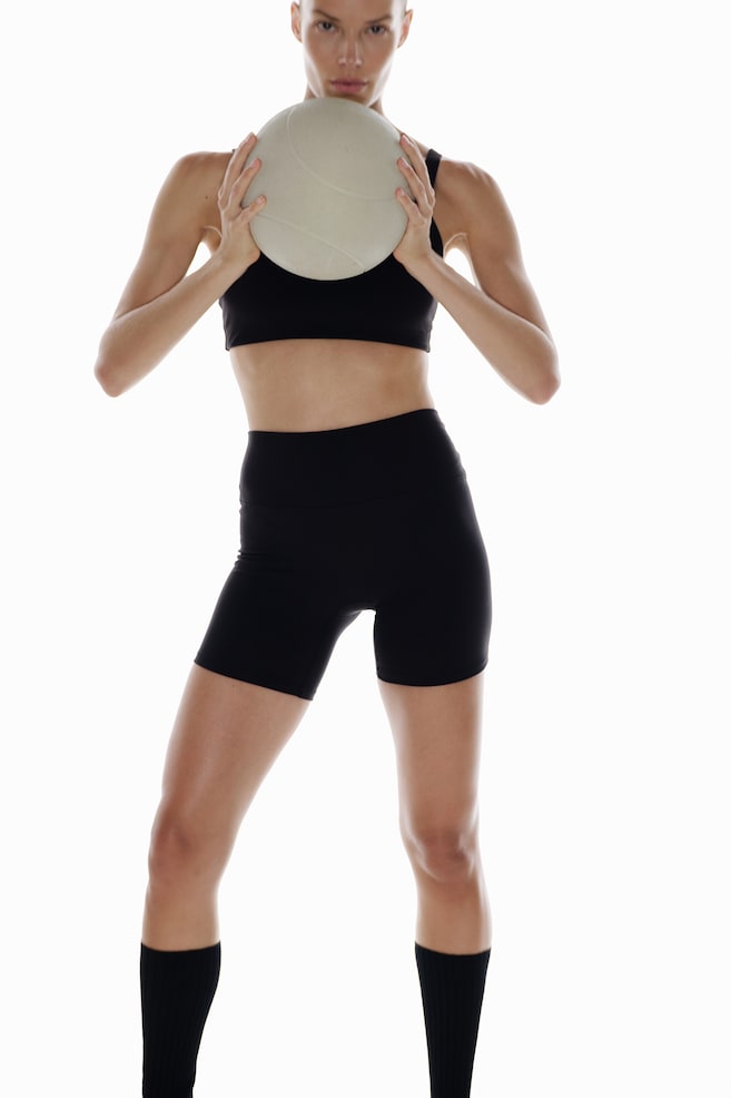 Modelul poartă pantaloni scurți de ciclism sportivi cu SoftMove®. Pantalonii scurți negri, cu talie înaltă, au o croială mulată și ajung până la jumătatea coapsei. - 1