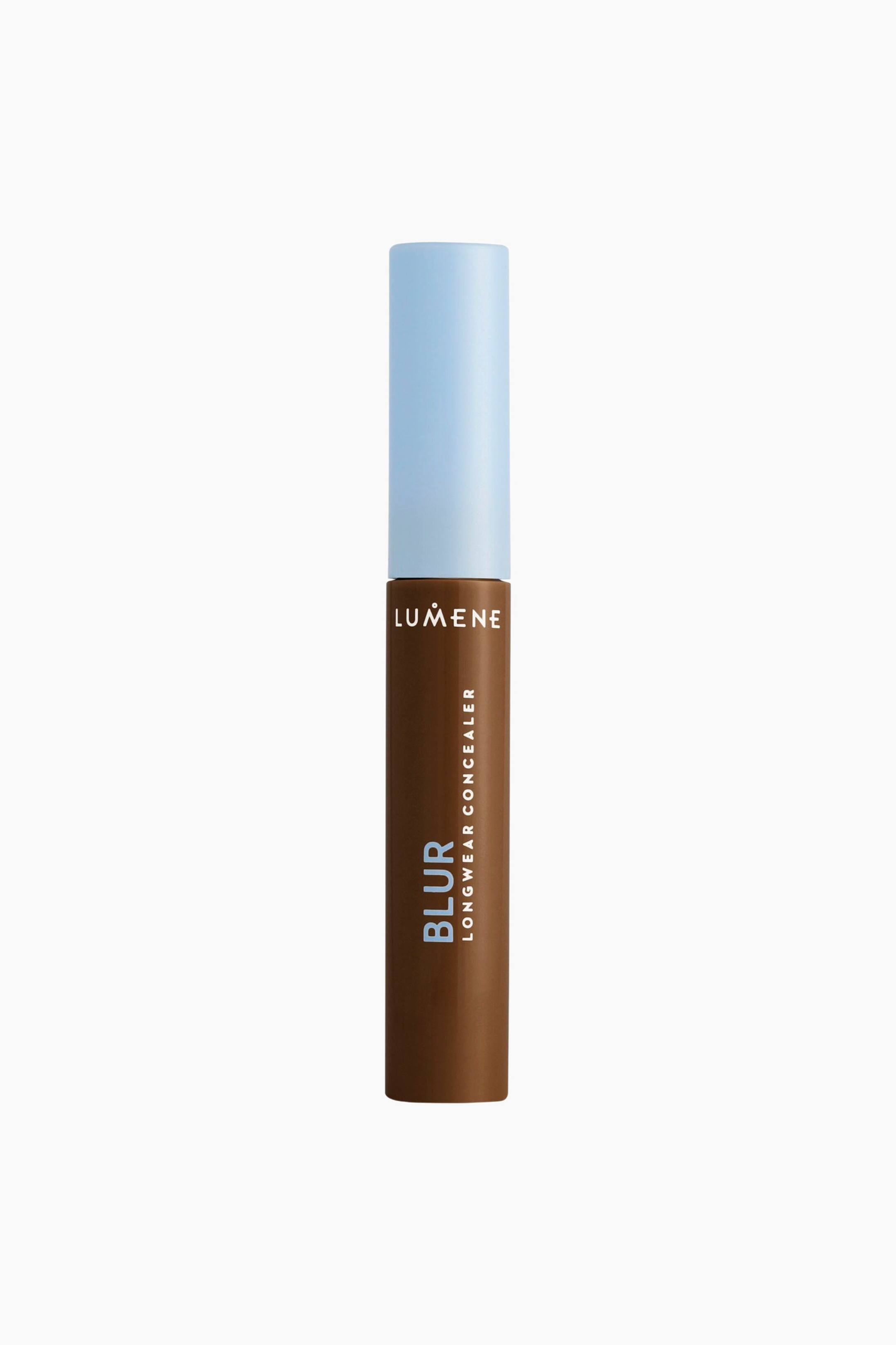 Visa större bild: Lumene Blur Longwear Concealer står upprätt och visar en cylindrisk tub i en mörkbrun nyans tillsammans med ett matt, ljusblått lock. På framsidan av tuben syns varumärkesnamnet ”LUMENE” i vitt högst upp, med ”BLUR” i ljusblått och ”LONGWEAR CONCEALER” i vitt, placerat vertikalt längs sidan.