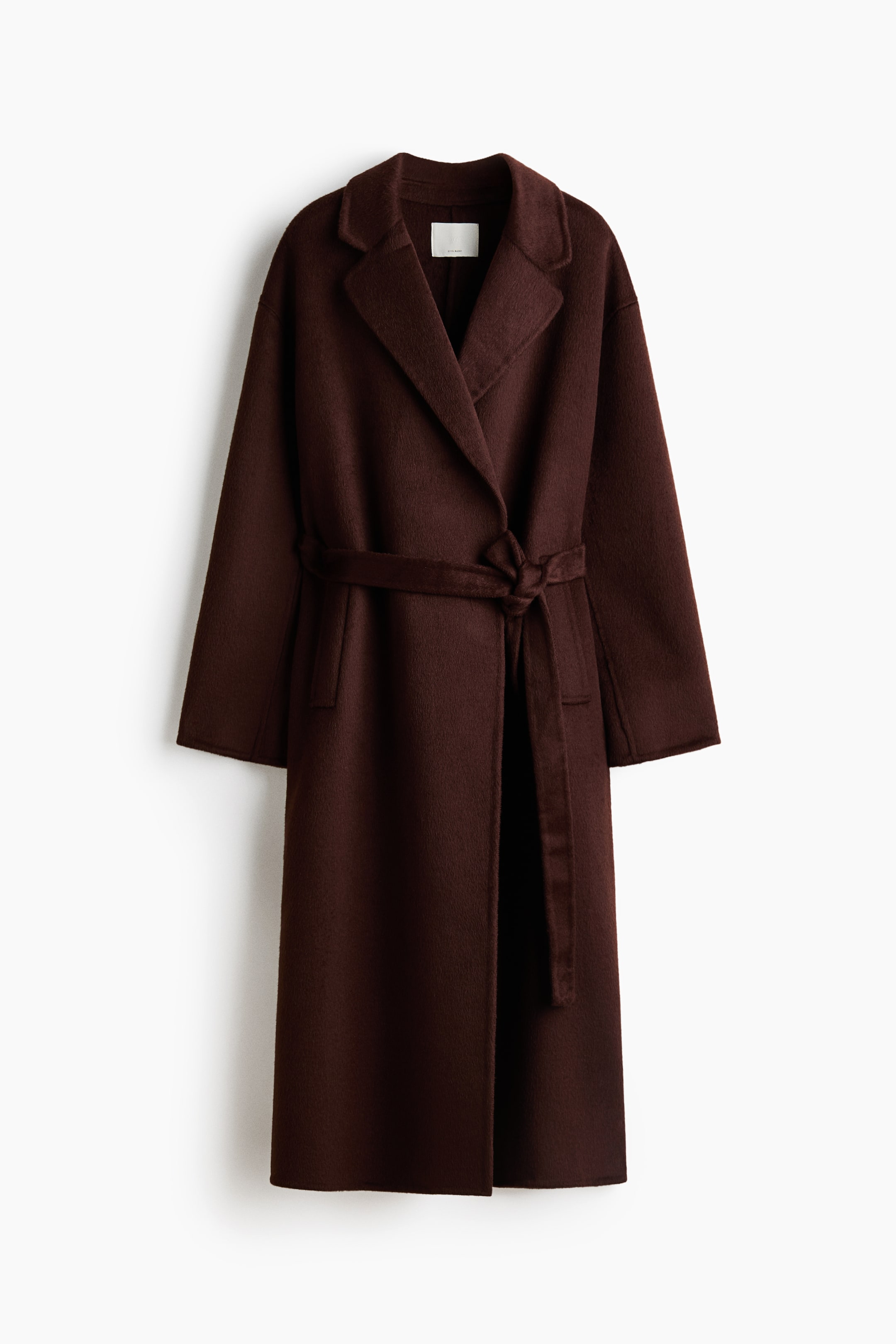 View larger image: A long, dark brown coat is hanging front-facing, featuring wide notch lapels, long sleeves, and a matching self-tie belt tied at the waist. The coat presents a relaxed silhouette with subtle side welt pockets and a textured fabric finish.