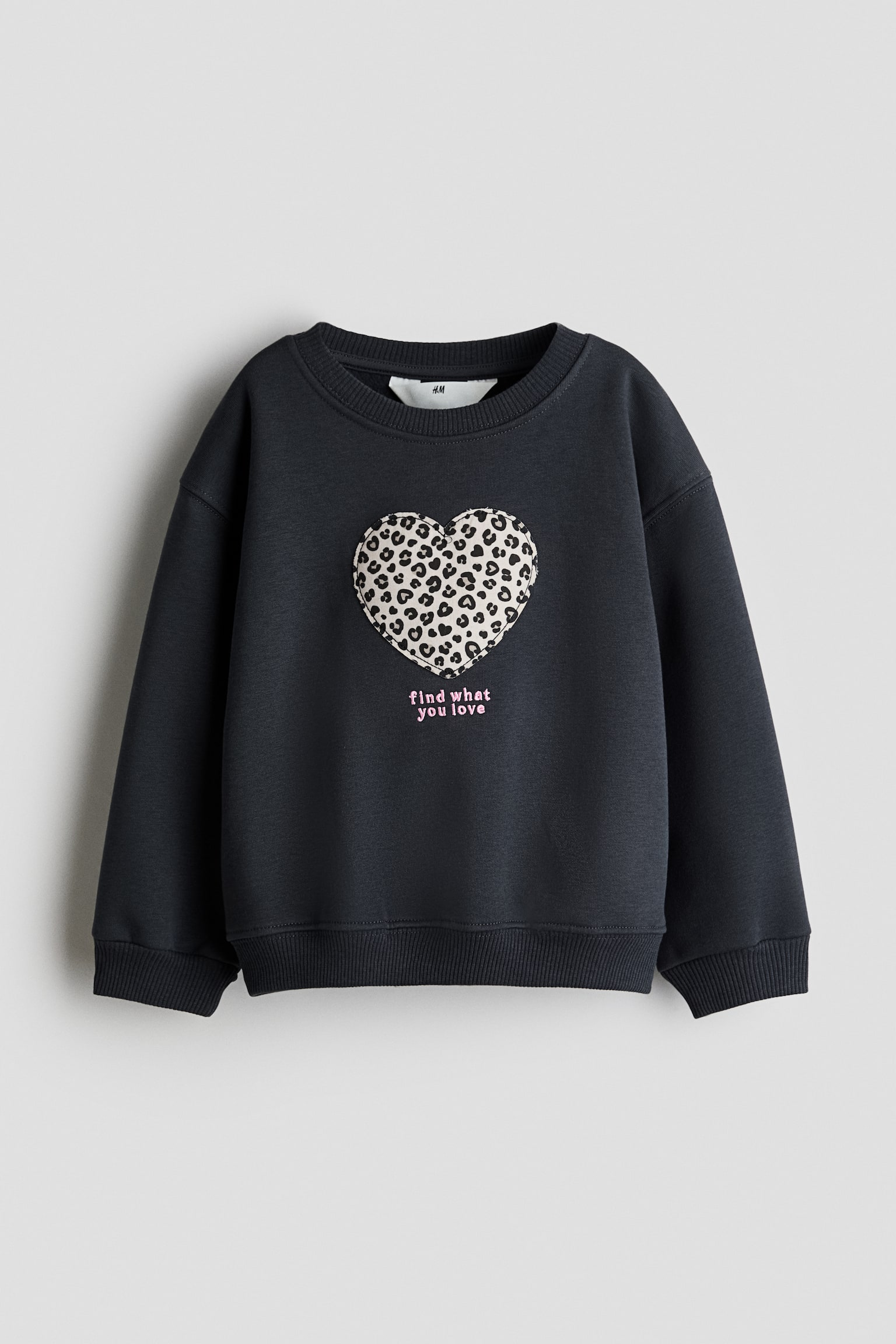 Ein dunkelgrauer Rundhals-Sweatshirt ist von vorne zu sehen und verfÃ¼gt Ã¼ber einen groÃen Leopardenmuster-HerzaufnÃ¤her, der mittig auf der Brust platziert ist, mit dem pink gestickten Schriftzug âfind what you loveâ darunter. Der Sweatshirt zeigt eine lockere Passform mit gerippten BÃ¼ndchen und geripptem Saum. - 1
