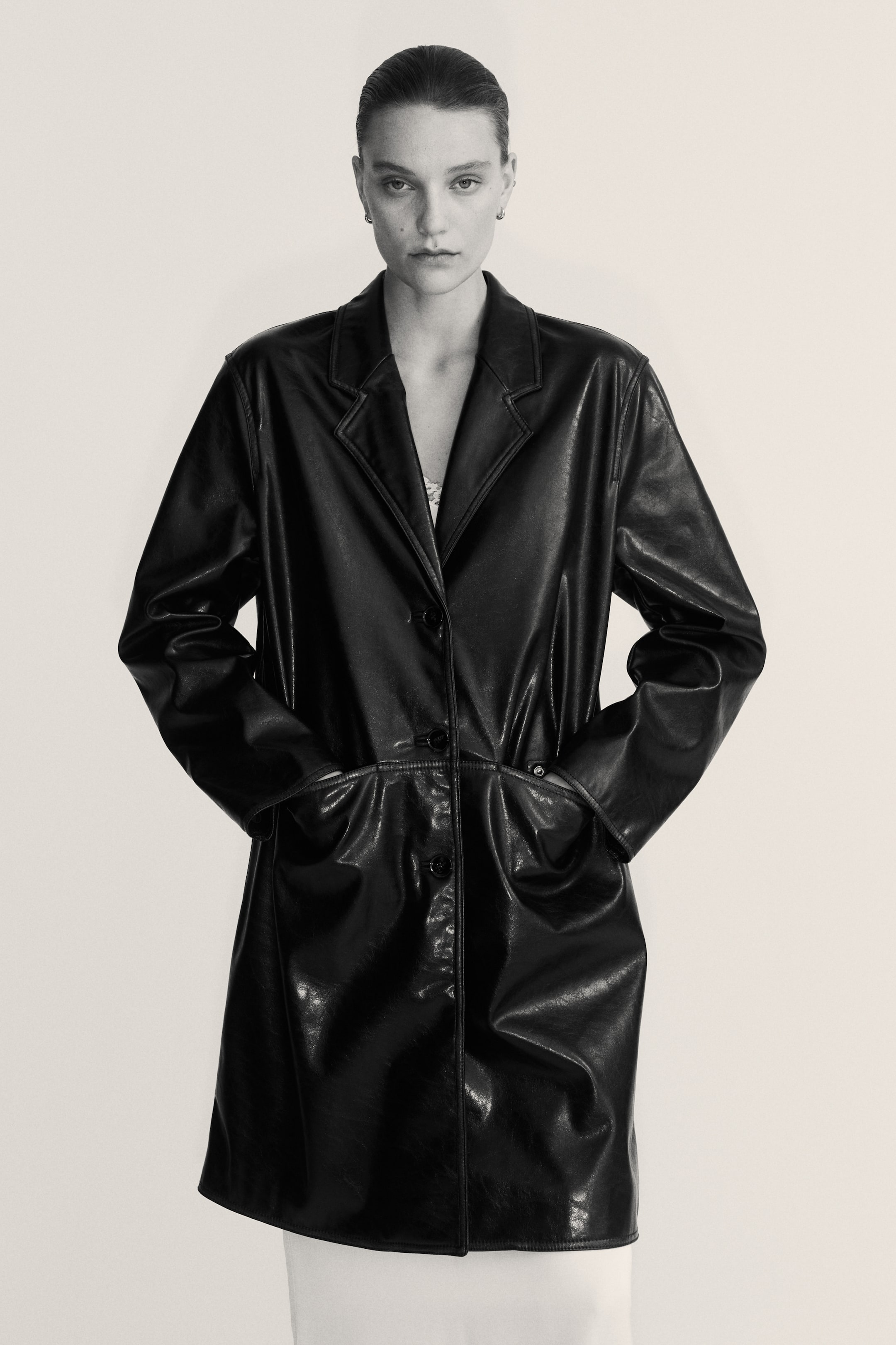 Agrandir l'image: Un manteau noir est présenté de FACE, avec une finition brillante et texturée. Il est conçu avec des revers crantés, une fermeture à trois boutons sur le devant et deux grandes poches plaquées.