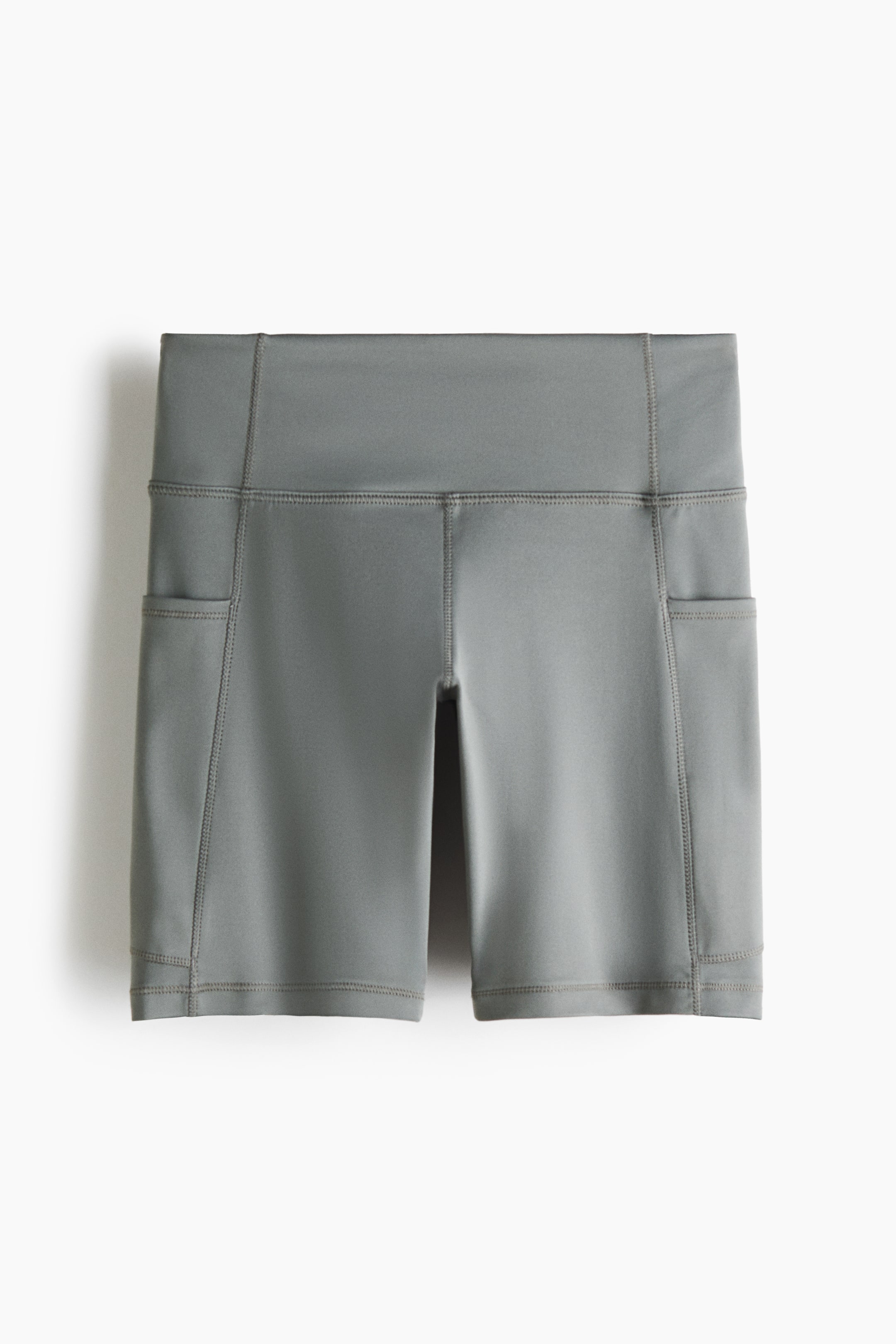 Größeres Bild ansehen: Die grauen Sport-Radshorts mit DryMove? werden in einer Vorderansicht präsentiert und zeichnen sich durch einen hohen, breiten Bund, sichtbare Flatlock-Nähte und Seitentaschen an beiden äußeren Oberschenkeln aus, die bis zur Mitte des Oberschenkels reichen.