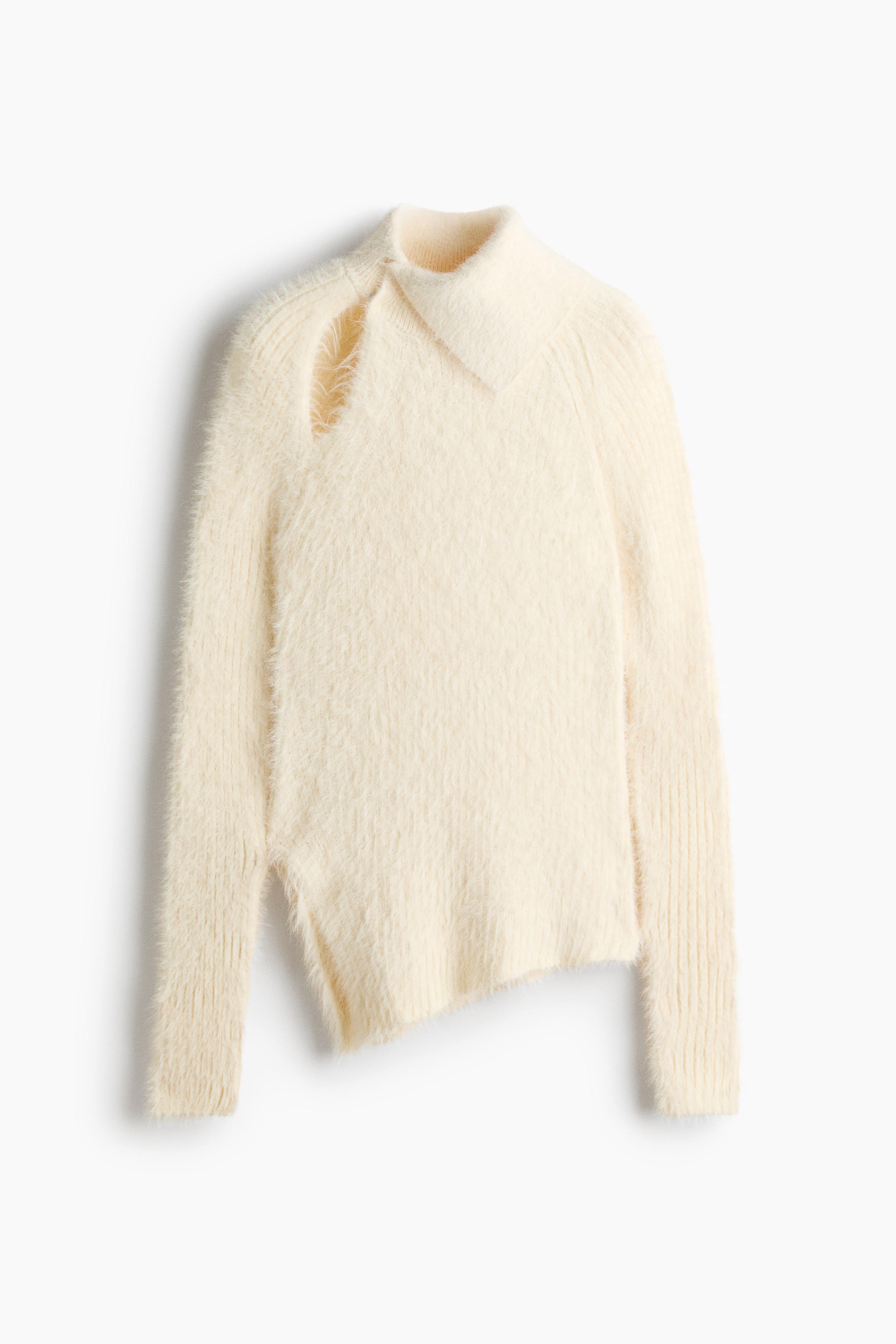 De model draagt een gebroken witte, fluffy gebreide trui, met een asymmetrische col, een uitsparing aan de voorkant van de schouder, lange raglanmouwen en een asymmetrische zoom. De trui is gestyled met zwarte leren broeken.