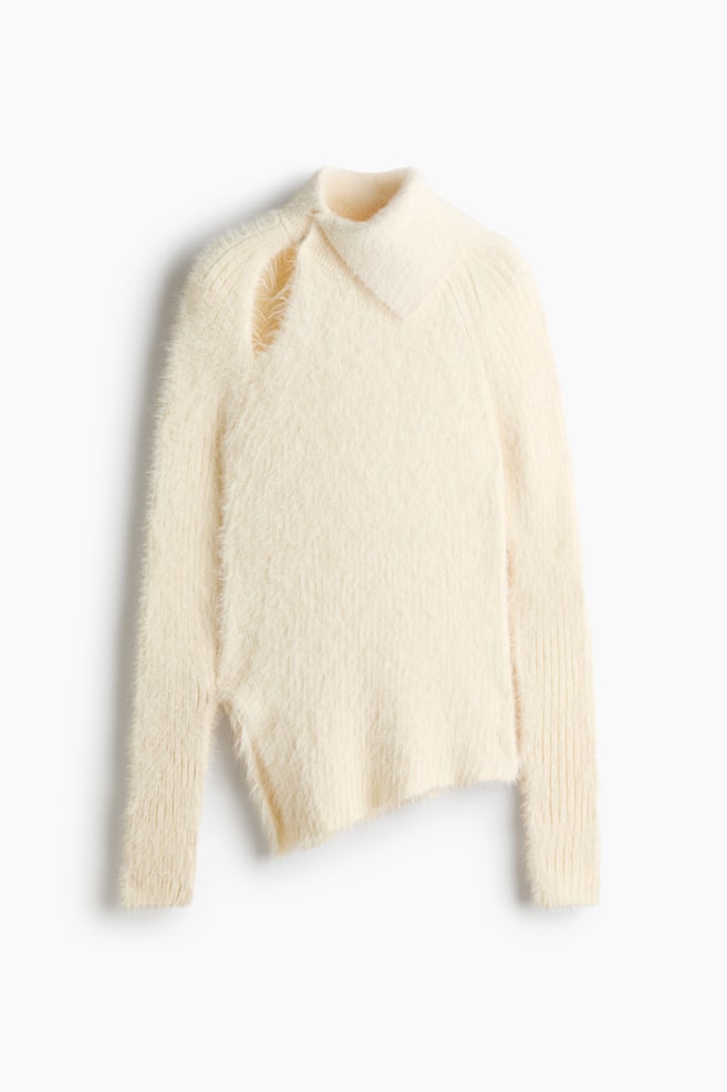 A cream-coloured jumper in a soft, fluffy knit is shown from the front, featuring an asymmetric roll neck and a teardrop-shaped cut-out on one shoulder. It has long raglan sleeves with ribbed cuffs and an asymmetric hemline with a slit at one side. - 1