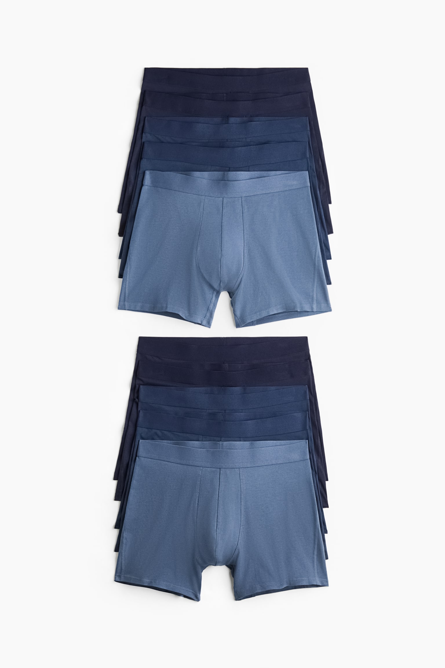 Ten pairs of menâs boxer briefs are arranged in two vertical stacks of five, displaying the front view in shades of blue ranging from dark navy to light slate blue. Each pair features a flat elastic waistband, a contoured front pouch with vertical seams, and short legs.