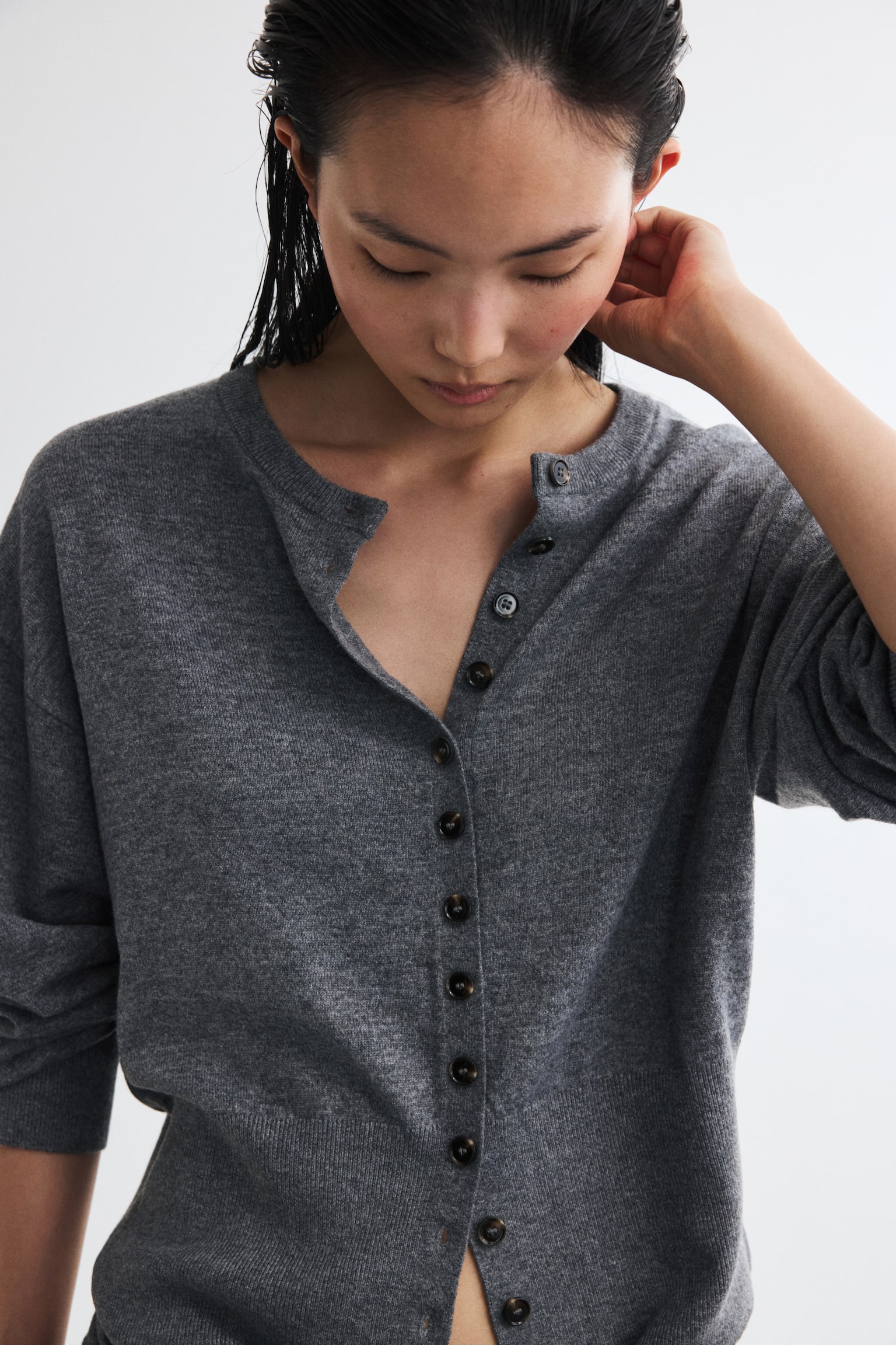 A heathered grey knit cardigan is facing front, showcasing a round neck and a full button-front fastening with small, dark brown buttons. It features long sleeves with ribbed cuffs and a ribbed hemline. - 1