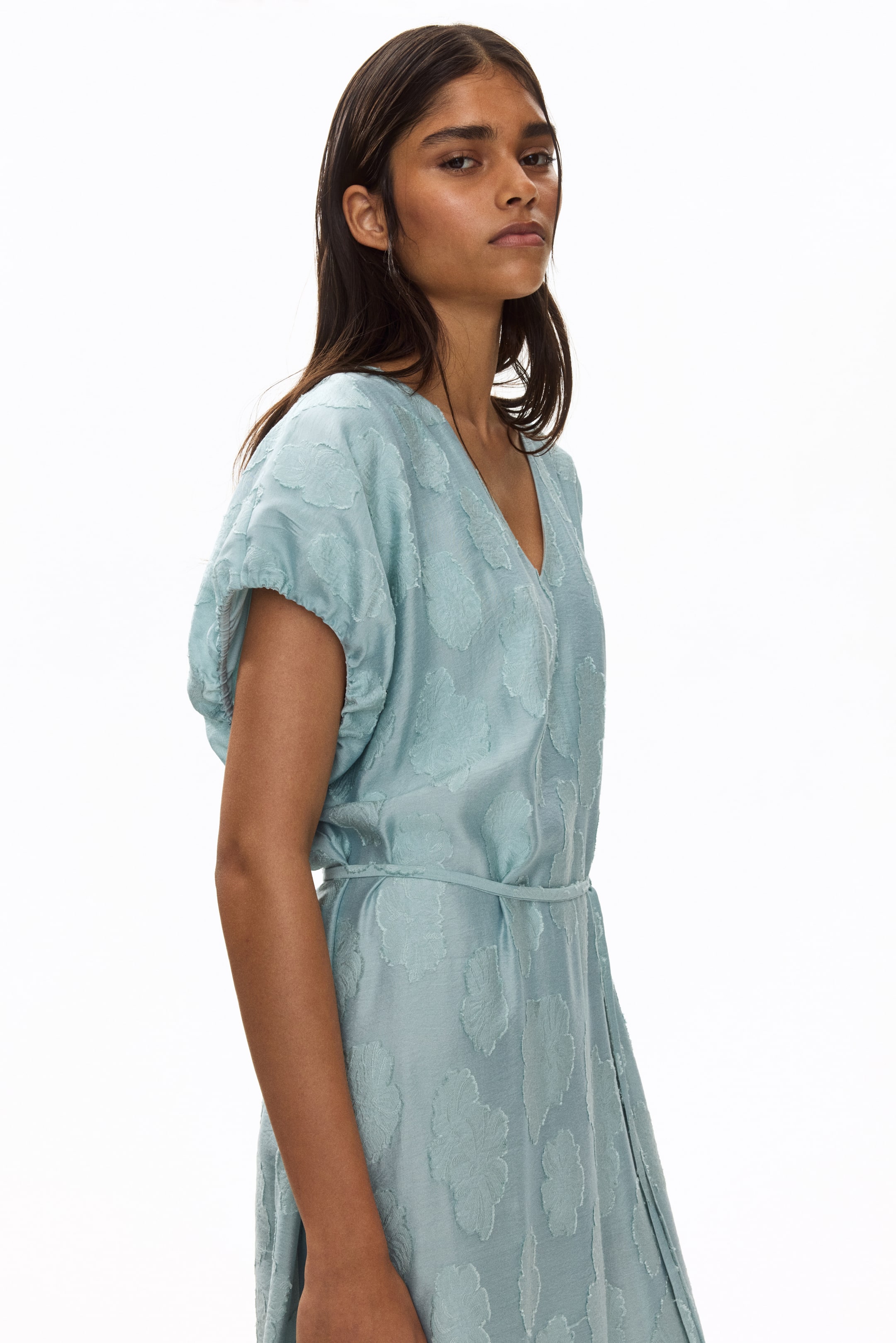 View larger image: A light blue dress showcasing a raised leaf pattern all over, a V-neckline, and gathered short sleeves. A self-fabric tie belt cinches the waist.