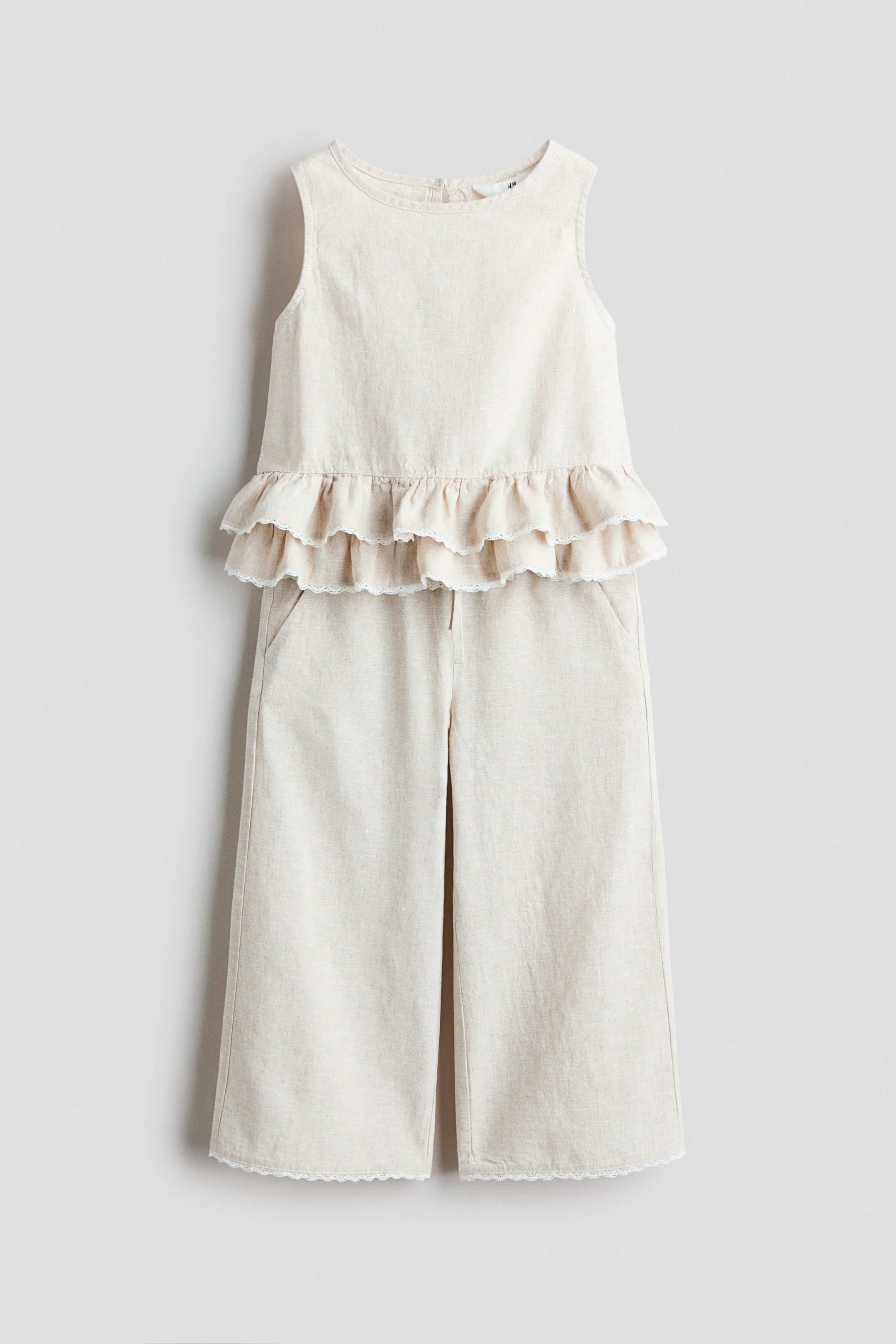 View larger image: "Presenting a light beige linen and cotton weave set from the front, this ensemble includes a sleeveless top and wide-leg trousers. The top showcases a round neckline and a tiered hem adorned with lace trims. Meanwhile, the trousers feature an elasticated drawstring waist, diagonal side pockets, and lace trims at the hem."