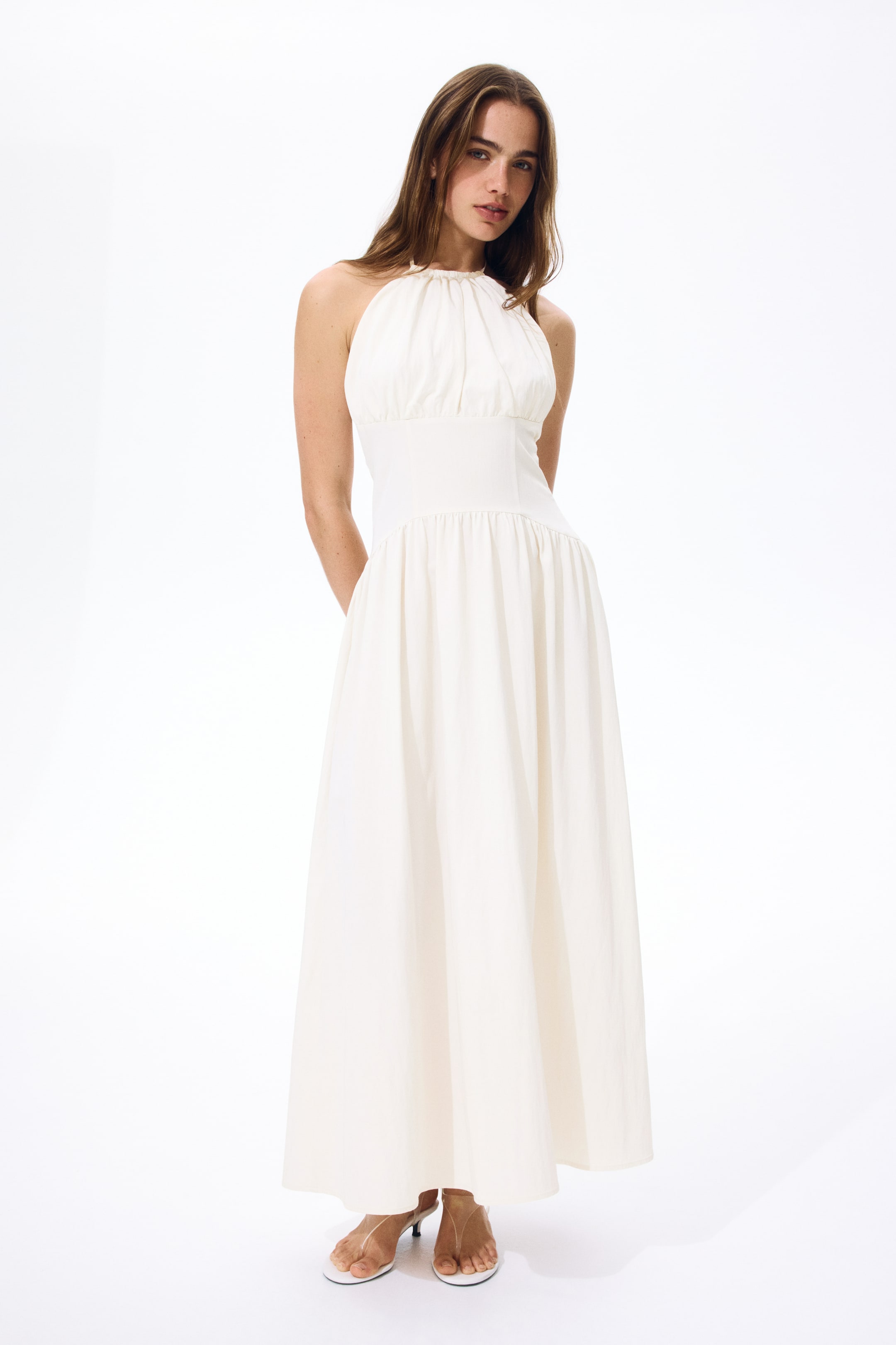 View larger image: The calf-length dress, displayed from the front, features a fitted bodice with a round, gathered halterneck and narrow ties threading through the neckline. A wide waist panel is included, with gathered seams above and below creating a ruched effect, and a gently flared skirt completes the design.