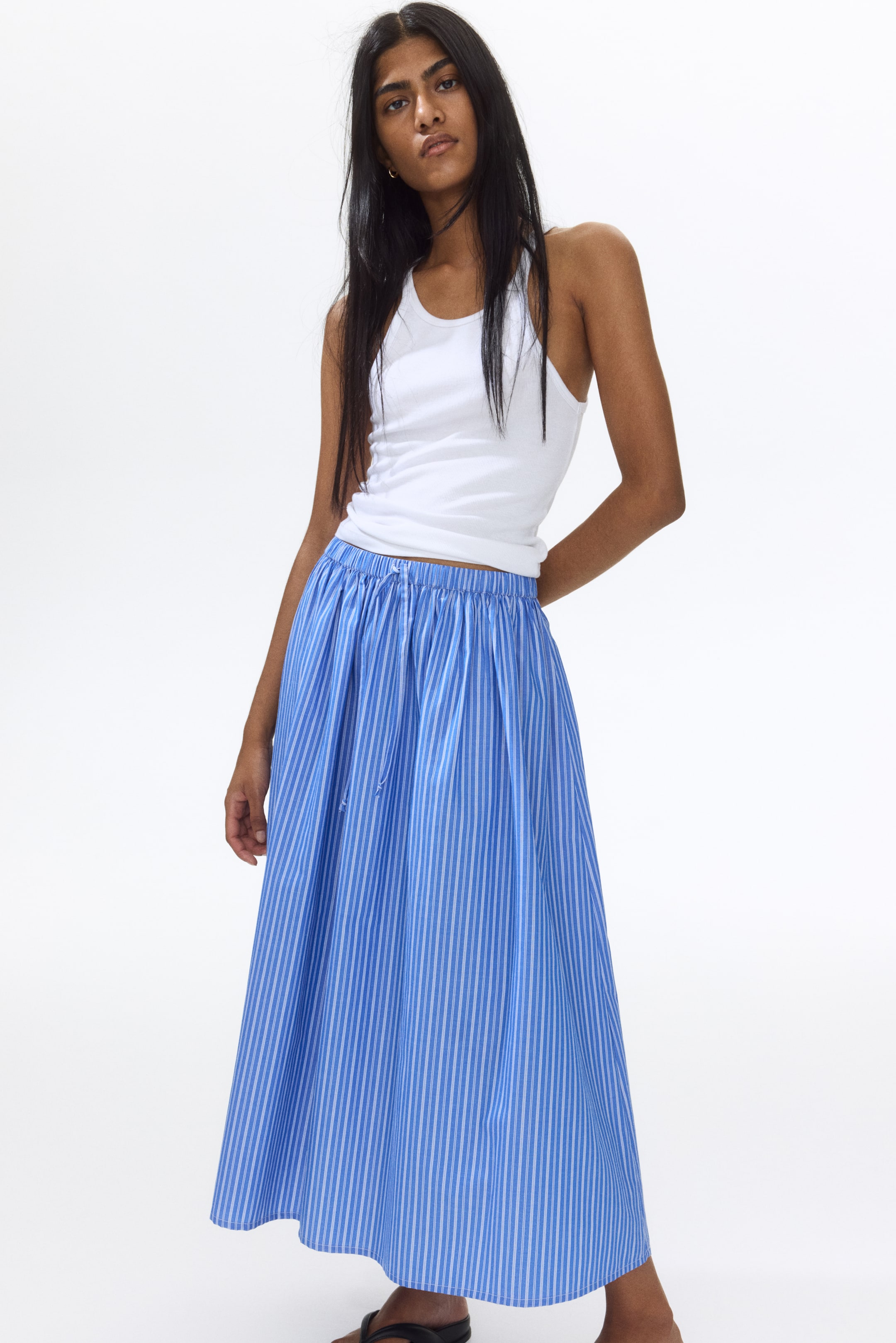 View larger image: A blue midi-length skirt showcasing thin white vertical stripes, gathering at an elasticized waistband with a visible drawstring, and flowing in an A-line silhouette, presented from a slight front-left angle.