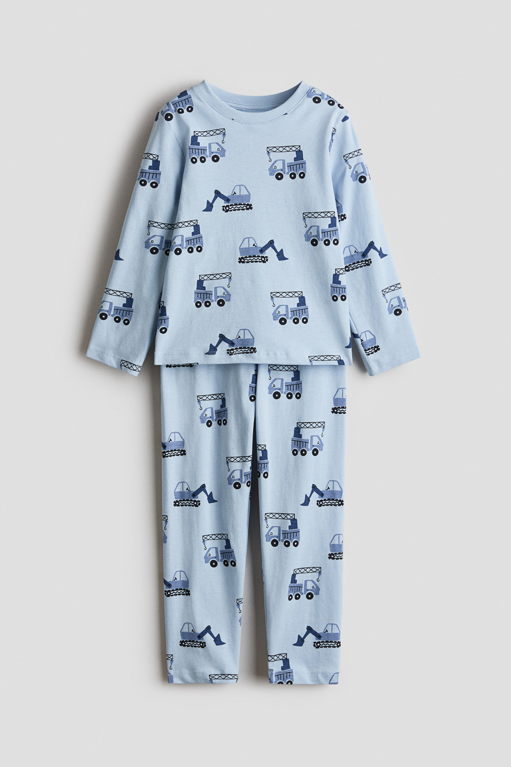 Agrandir l'image: Un ensemble de pyjama pour enfants est posé à plat, affichant un haut à manches longues bleu clair avec un col ras du cou et un pantalon assorti de pleine longueur. L'ensemble présente un motif répétitif de véhicules de construction bleu foncé, comprenant des excavatrices, des camions-bennes et des grues.