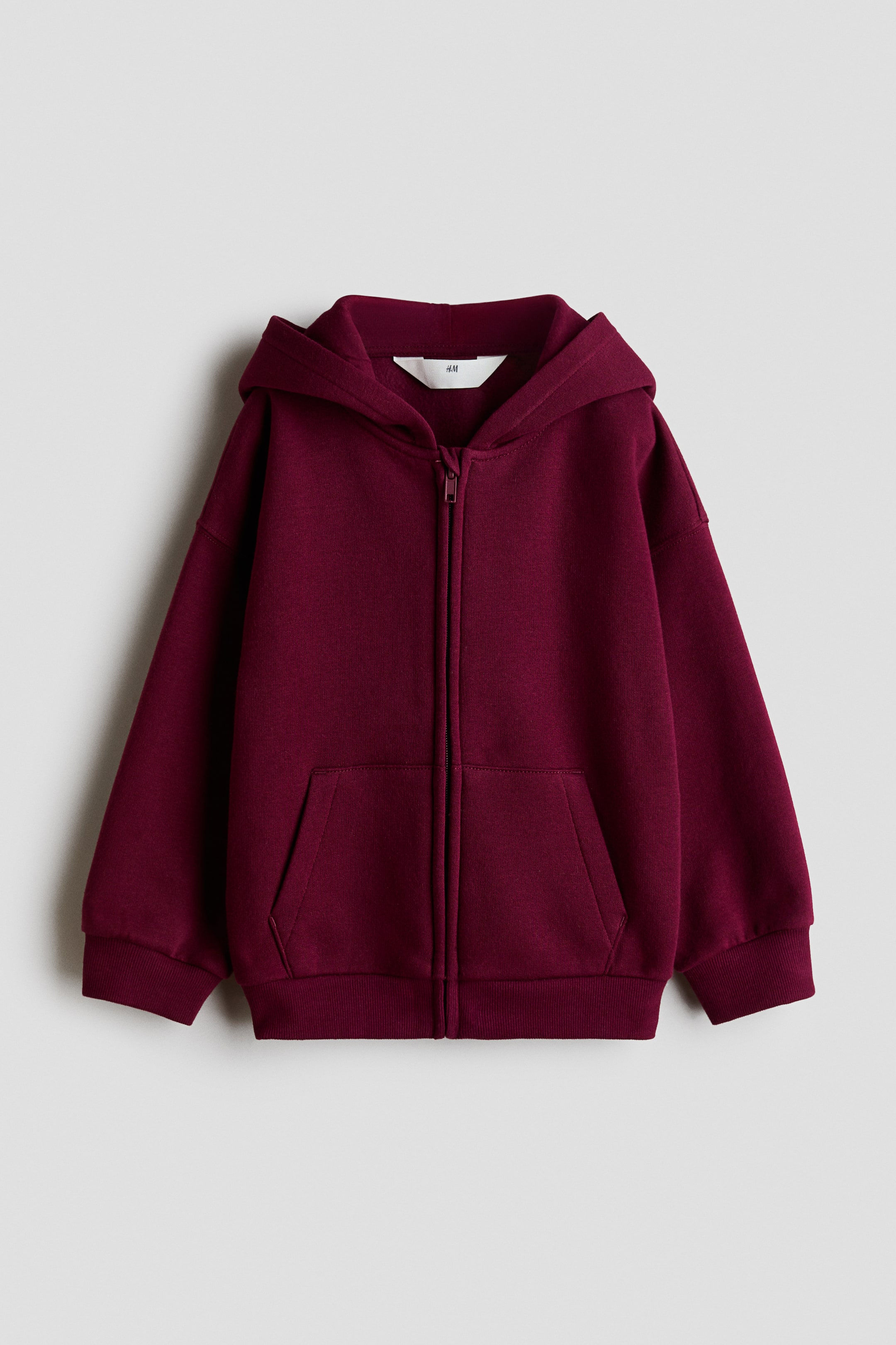 Grösseres Bild ansehen: Ein übergroßer bordeauxroter Hoodie mit durchgehendem Reißverschluss ist nach vorne gerichtet und zeigt einen durchgehenden Reißverschluss, ein sichtbares Kapuzenfutter und zwei aufgesetzte Fronttaschen. Er zeichnet sich durch überschnittene Schultern, gerippte Bündchen und einen gerippten Saum aus.