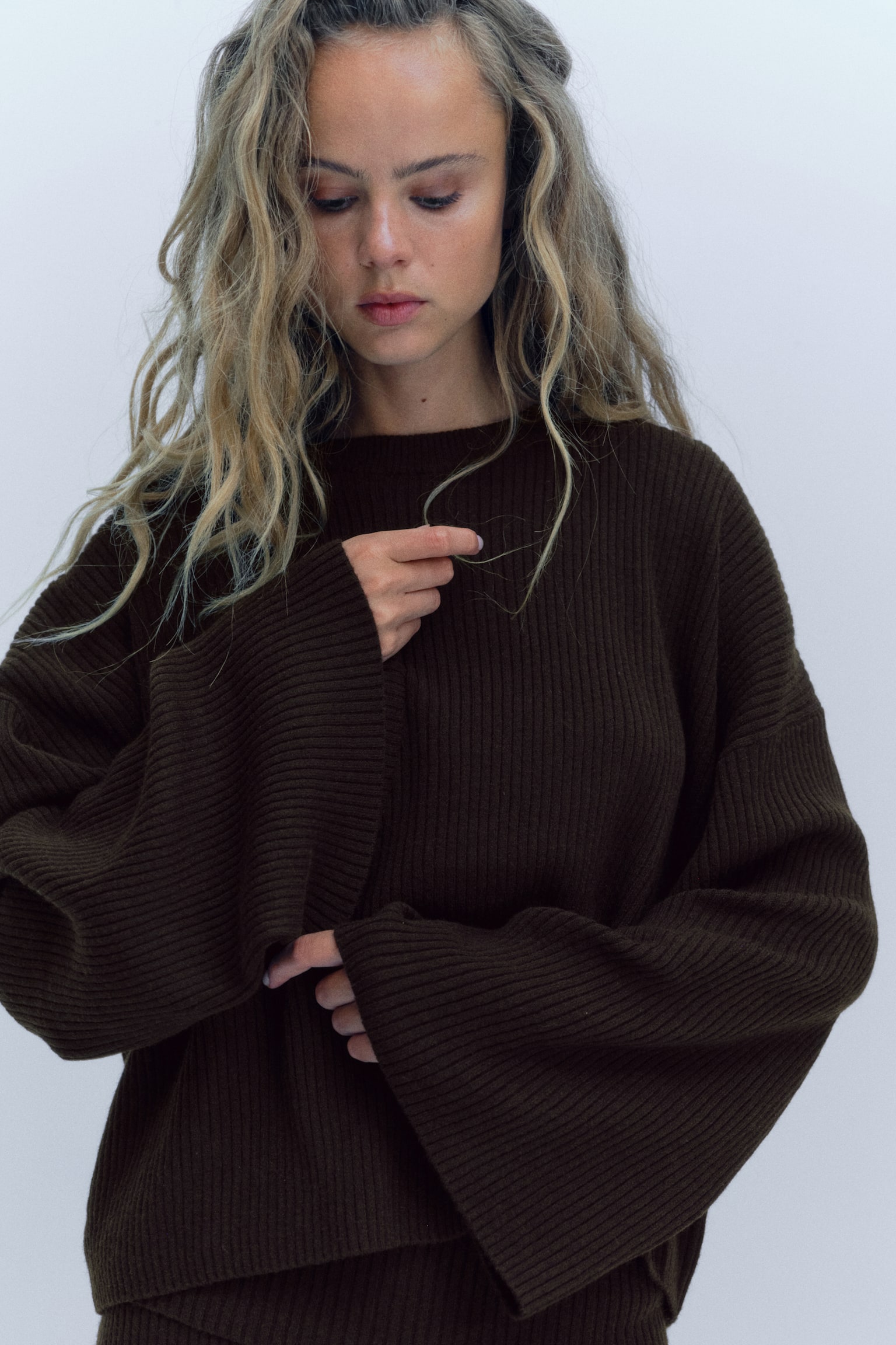 The dark brown ribbed knit jumper is laid flat and front facing, featuring a round neckline and long, wide sleeves with unbanded hems. - 1