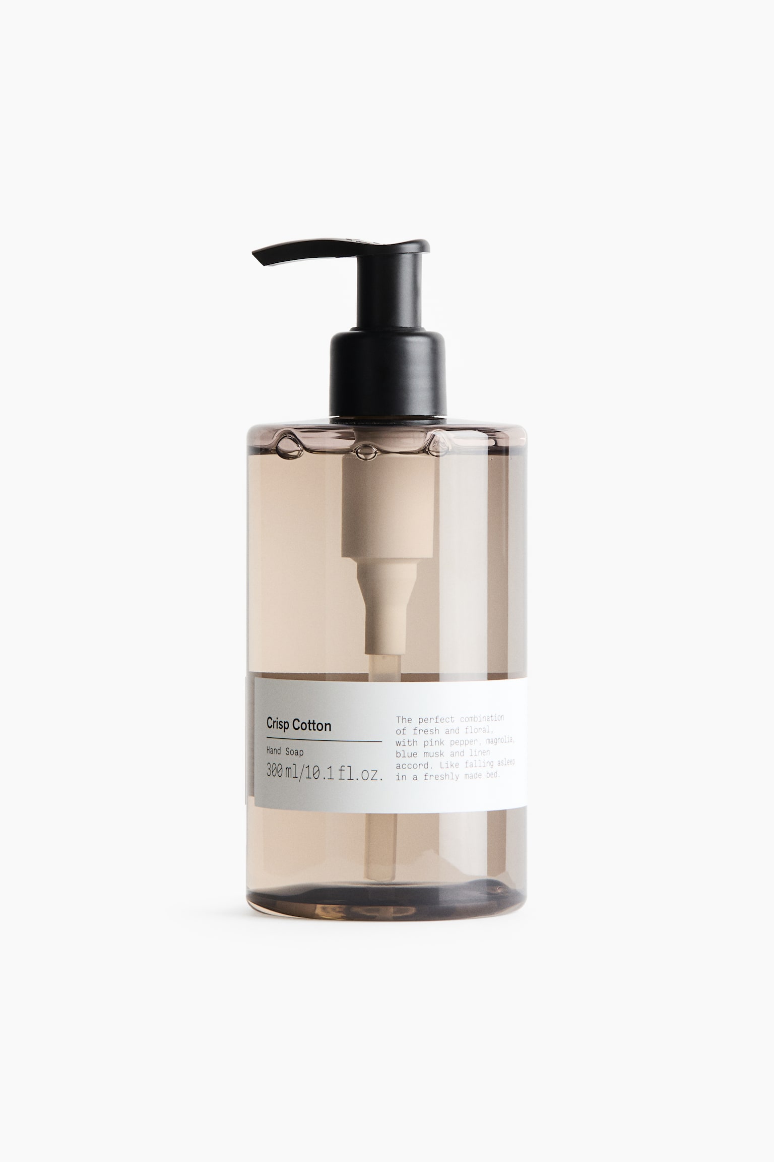 A cylindrical bottle of Crisp Cotton hand soap is standing upright, facing front, featuring a translucent, tinted brown plastic body filled with clear liquid. The bottle is topped with a black pump dispenser and features a white paper label wrapped around the lower half displaying the product name, volume, and description in black text.