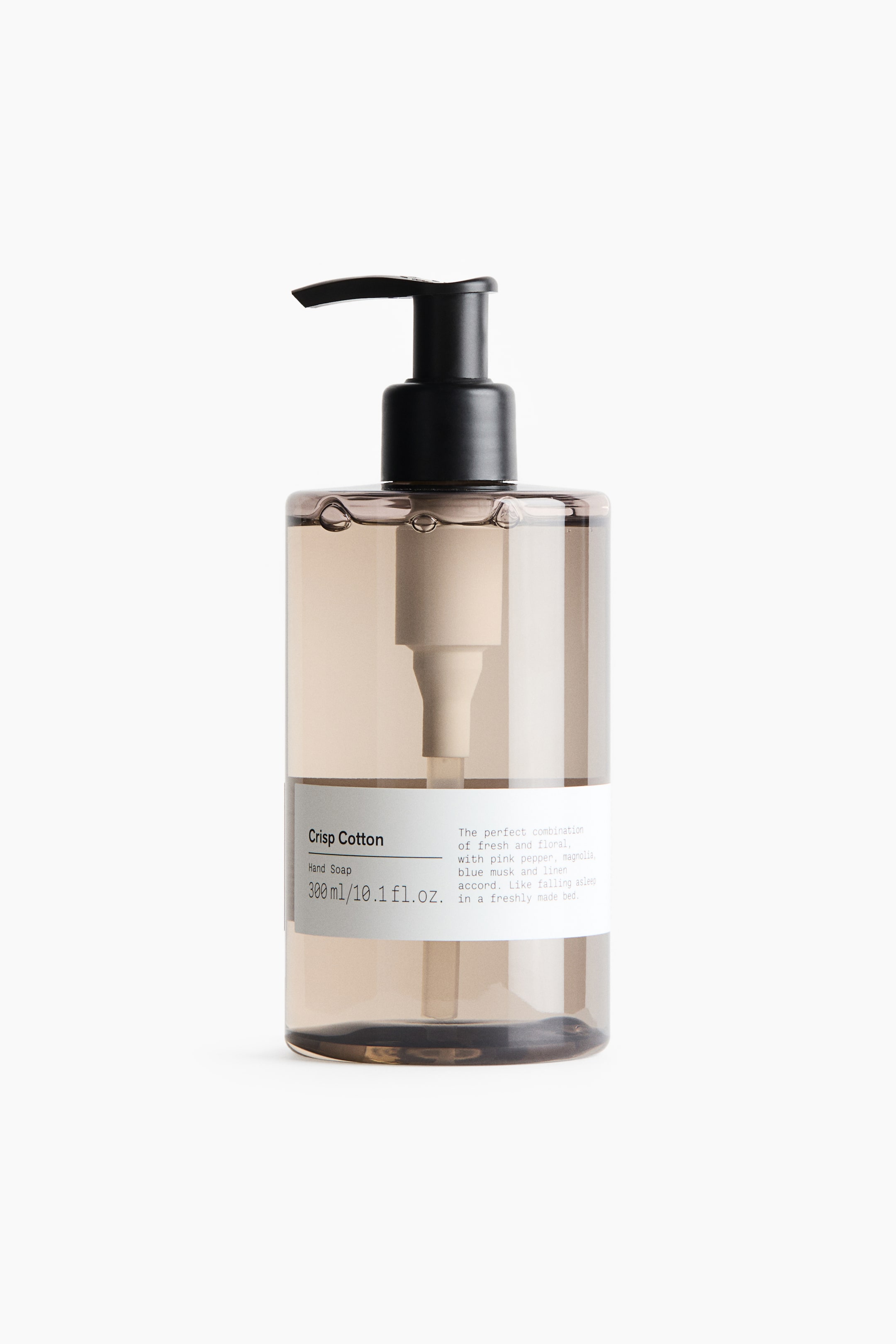 View larger image: A cylindrical bottle of Crisp Cotton hand soap stands upright, facing forward, featuring a translucent, tinted brown plastic body filled with clear liquid. The bottle is topped with a black pump dispenser and features a white paper label wrapped around the lower half, displaying the product name, volume, and description in black text.