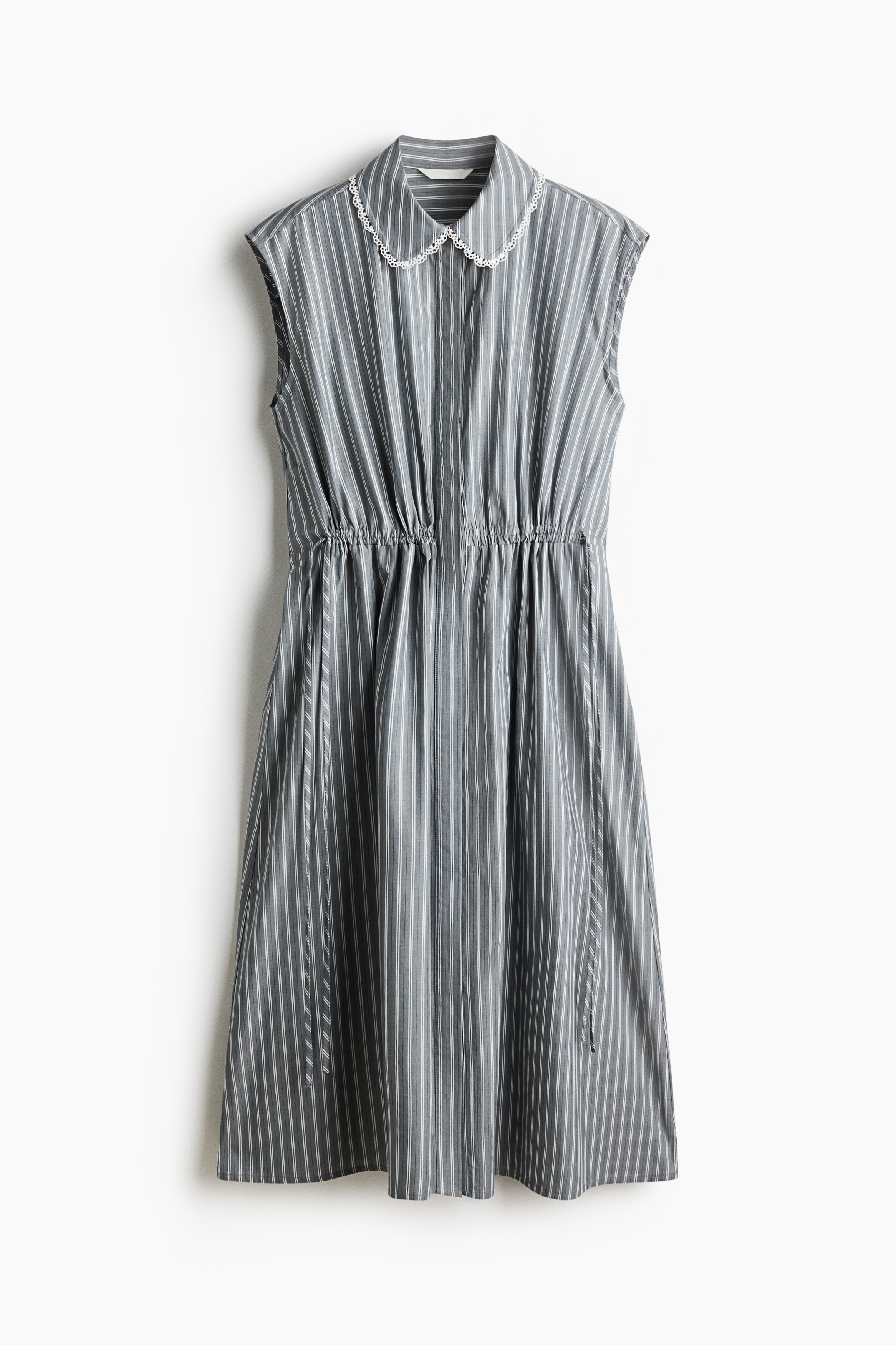 A calf-length, sleeveless dress in a blue and white vertical stripe pattern is being worn by the model. The dress features a white lace-trimmed collar, a drawstring waist tied at the sides, and a gently flared skirt styled with black flat shoes.