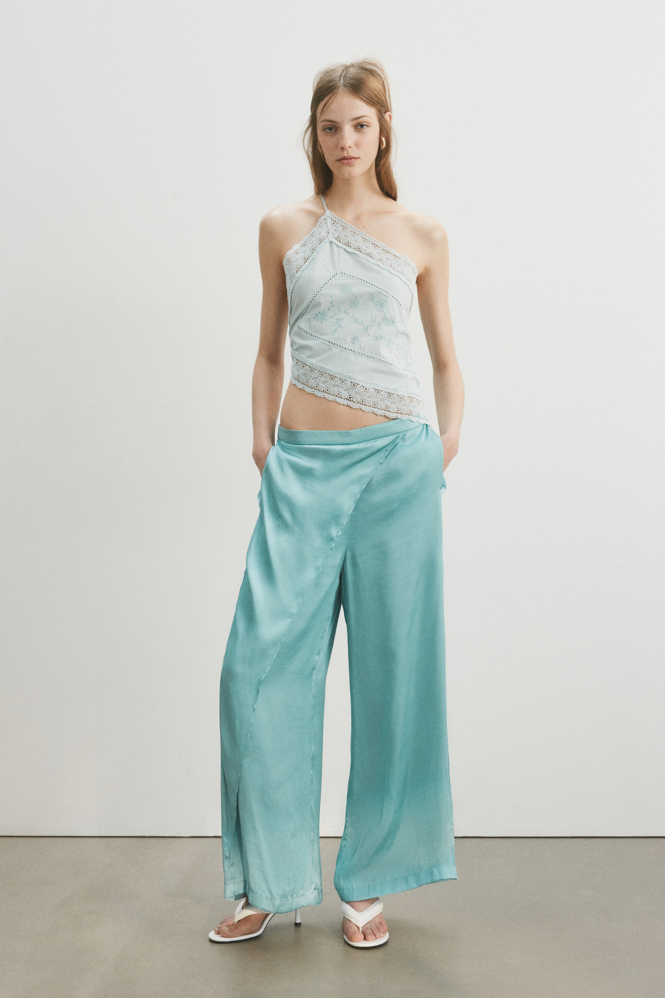 View larger image: "Ang wide-leg trousers na gawa sa malambot na satin na may nakatahing wrap detail sa harap ay suot ng model, na naglalagay ng kanyang mga kamay sa mga bulsa ng trousers."