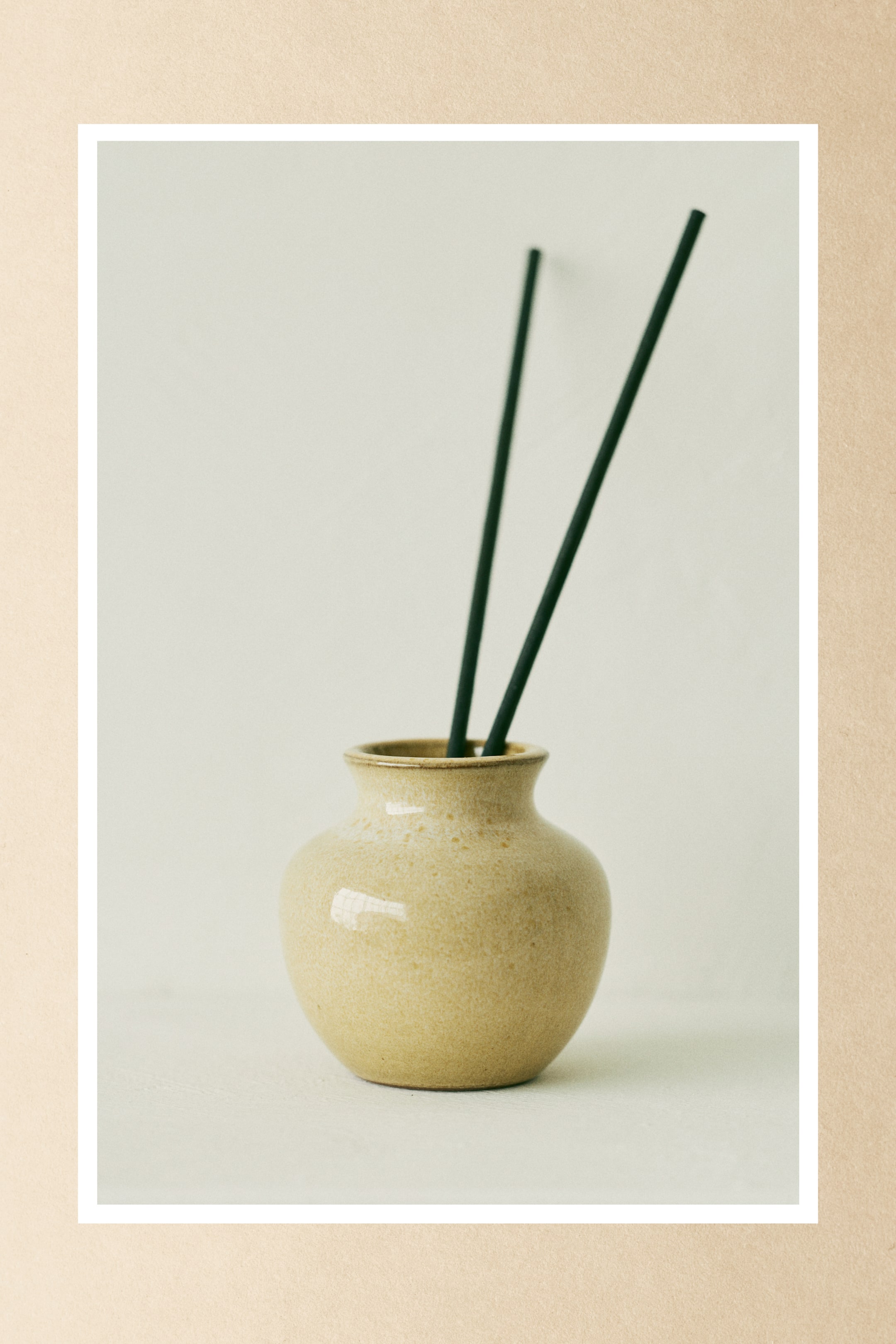 הצגת תמונה גדולה יותר: שני קנים דקים בצבע כהה, העשויים מנייר מבושם, עומדים זקופים בתוך אגרטל קרמי קטן בצבע בז' בהיר, בעל גוף מעוגל ופתח צר ומתרחב.