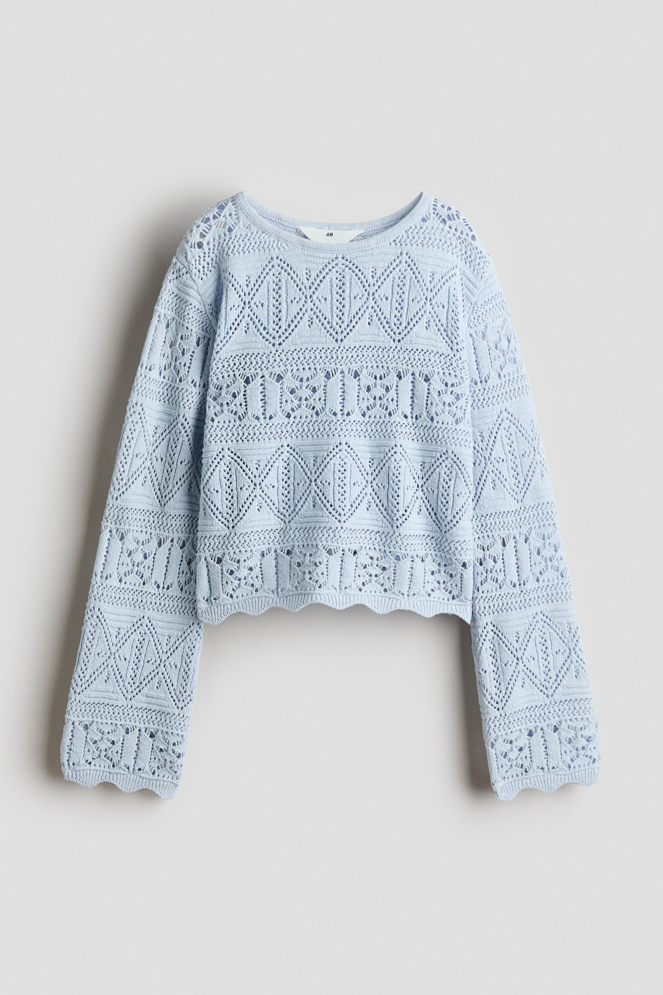 View larger image: A light blue sweater showcases its front, highlighting an open-knit design with geometric patterns across the body and long sleeves, a round neckline, and a scalloped cropped hem.