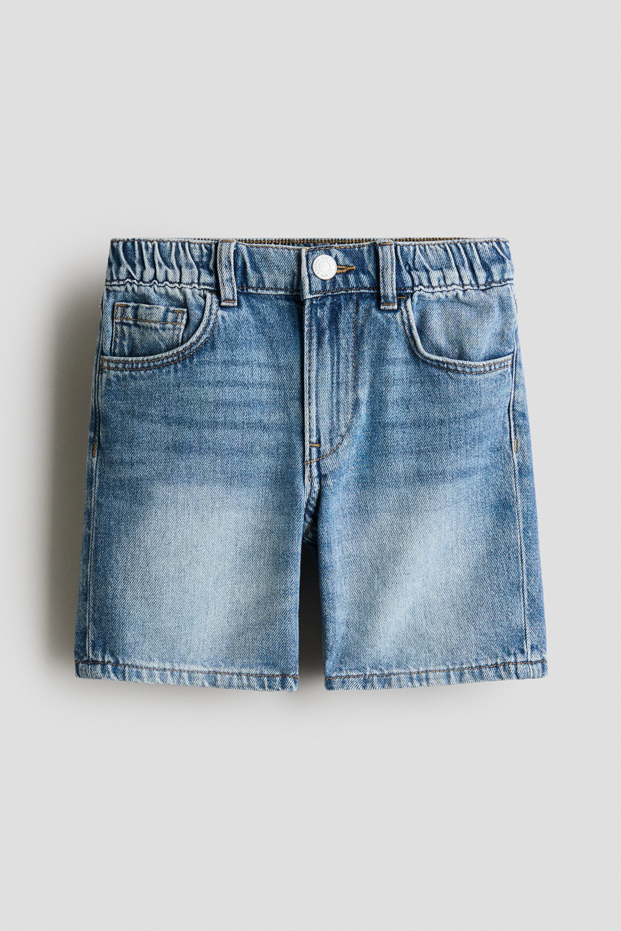 Grotere afbeelding bekijken: Lichtblauwe, gewassen denimshorts tonen hun voorzijde en beschikken over een elastische achtertailleband, riemlussen, een witte knoopsluiting en twee gebogen voorzakken met een muntzakje. Fading en whiskering zijn zichtbaar op de dijen.