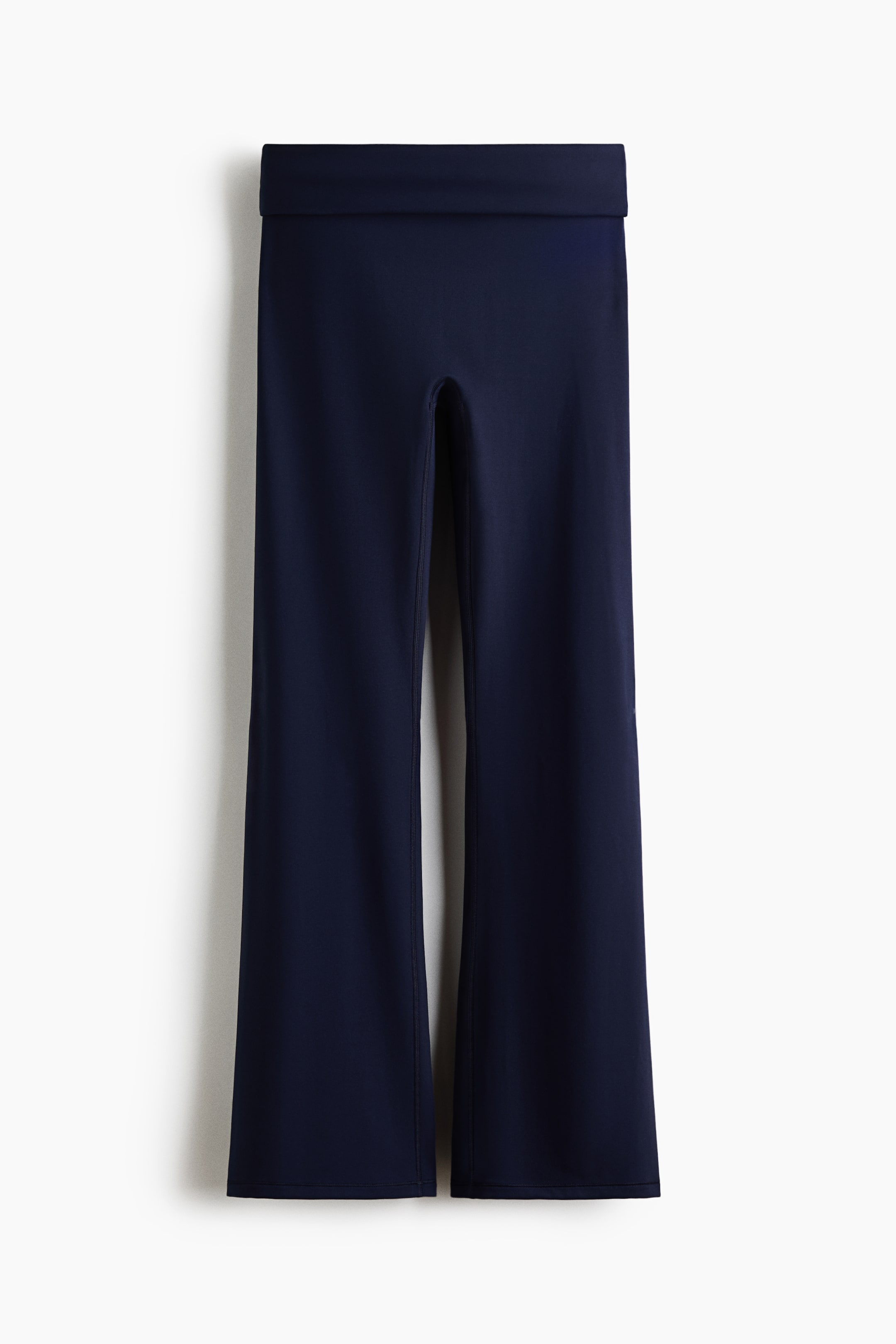 View larger image: Flared yoga leggings are shown in a dark navy blue colour, featuring a wide, flat waistband. The legs fit closely through the thigh and flare out significantly from the knee down, presented from the front.