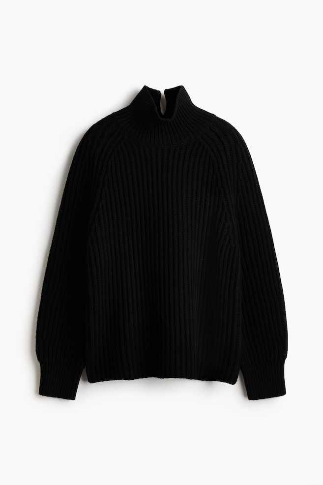 A black ribbed-knit sweater is hanging facing the front, featuring a high mock neck, raglan sleeves, and long ribbed cuffs. The sweater is showcasing an all-over vertical rib pattern and a relaxed-fit silhouette. - 1