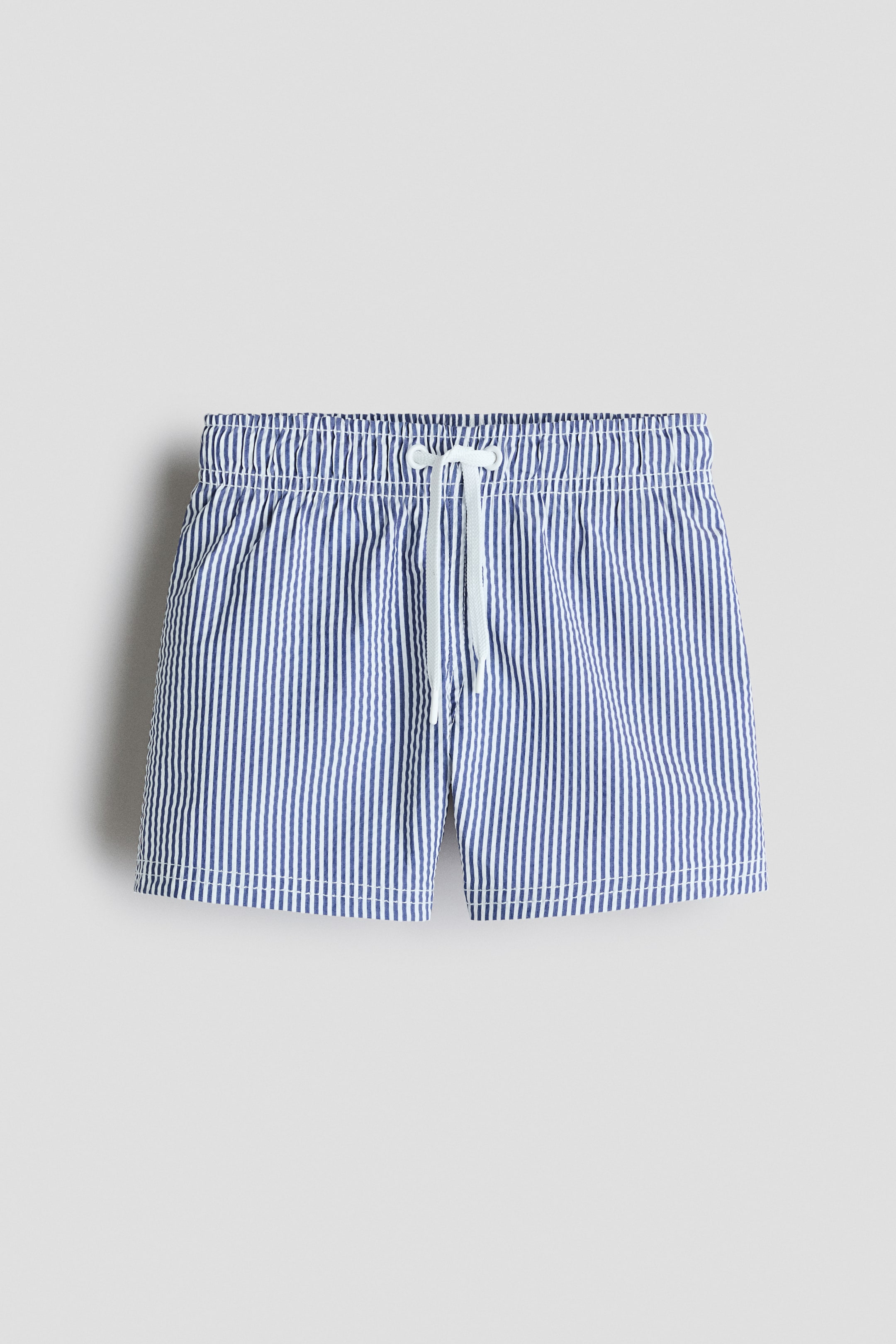 View larger image: The swim shorts are shown in a front view, showcasing blue and white vertical stripes, an elastic waistband, and a white drawstring tied at the front.