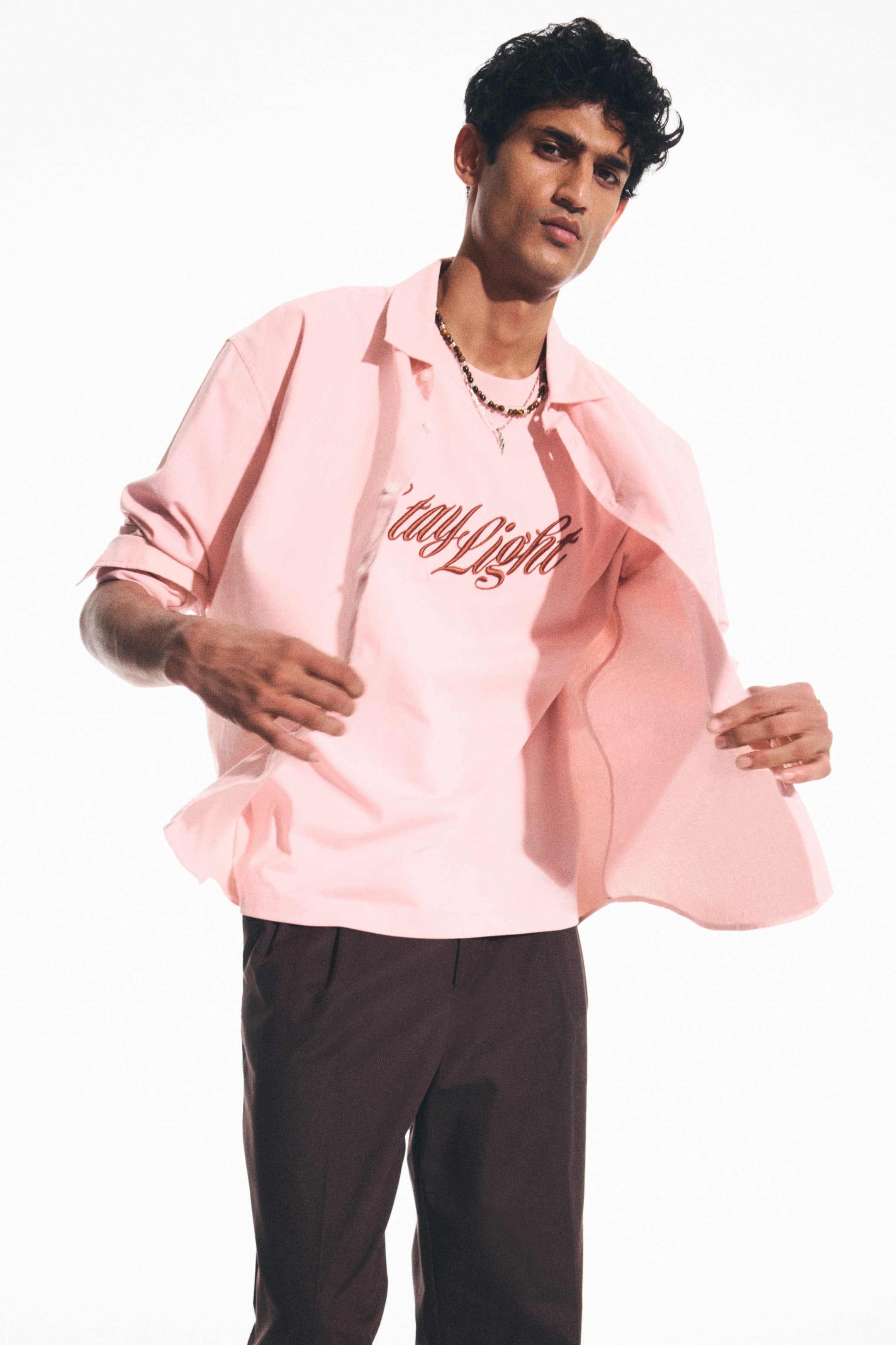 View larger image: The model is sporting a pink T-shirt featuring a round neckline, adorned with red script text reading 'stay light' across the front. She is showcasing a pink overshirt, worn open to reveal the T-shirt layered underneath.