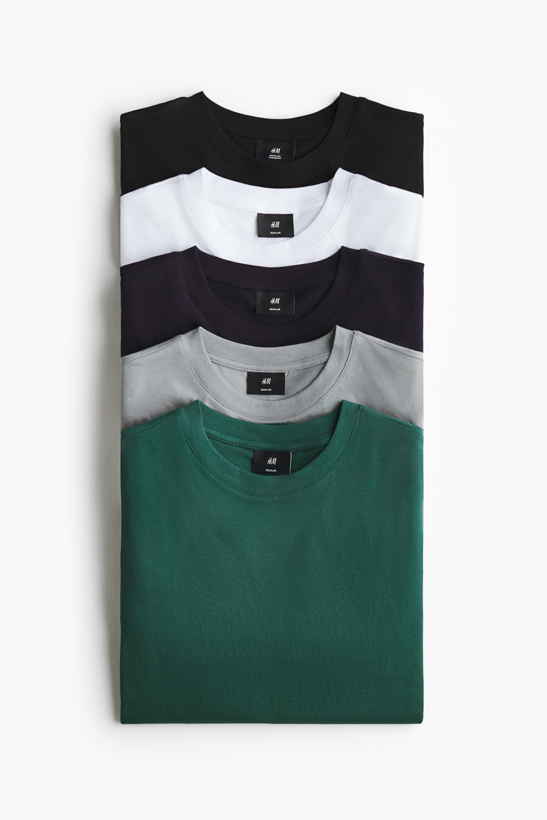View larger image: Five folded cotton jersey t-shirts are stacked vertically from a front angle, showcasing their round, rib-trimmed necklines in black, white, dark purple, grey, and forest green.
