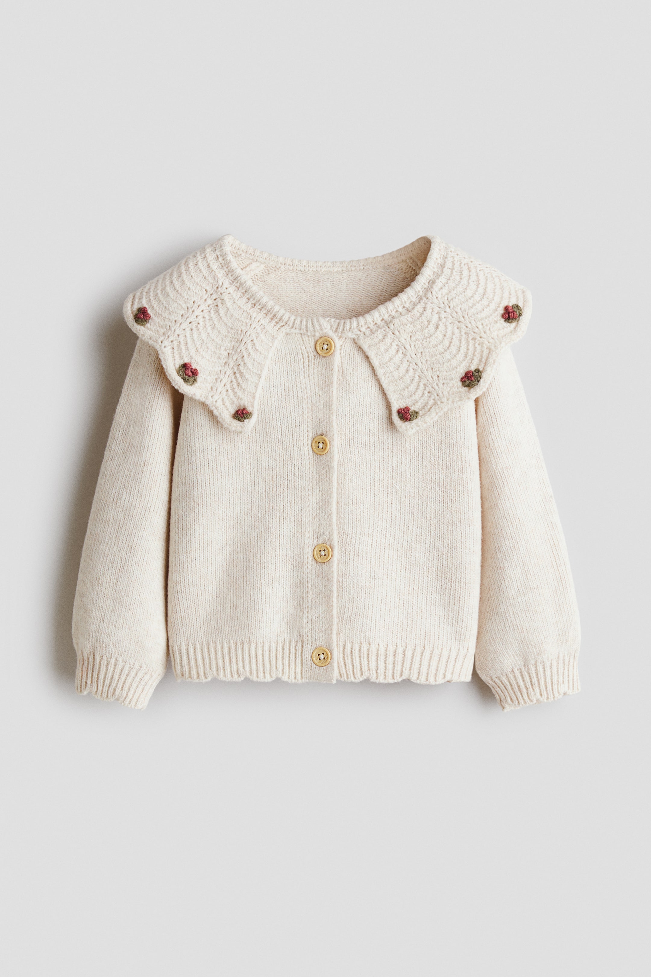 Ver imagen más grande: El cárdigan de punto en color crema presenta un gran cuello con borde ondulado, adornado con pequeños detalles florales bordados. Cuenta con cinco botones de color claro en la parte delantera y está diseñado con puños acanalados y bajo ondulado.