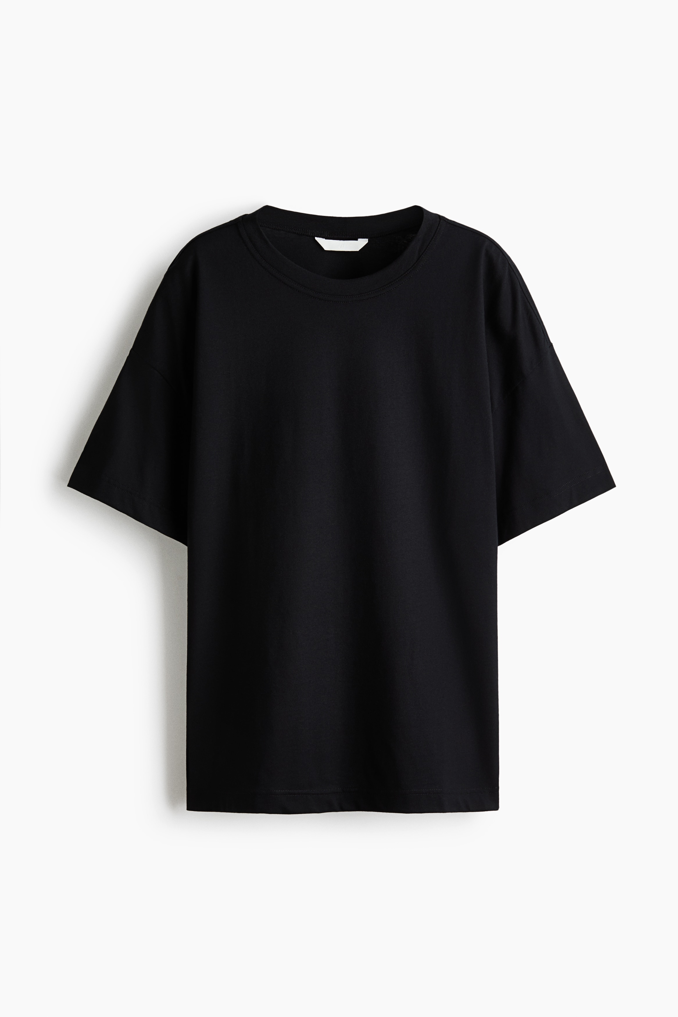 Ein schwarzes, übergroßes T-Shirt wird von vorne präsentiert, mit einem Rundhalsausschnitt und kurzen Ärmeln, die hochgekrempelt getragen werden. Darunter wird sichtbar ein weißes, langärmeliges Hemd getragen, und das T-Shirt wird mit dunklen, weit geschnittenen Jeans kombiniert.