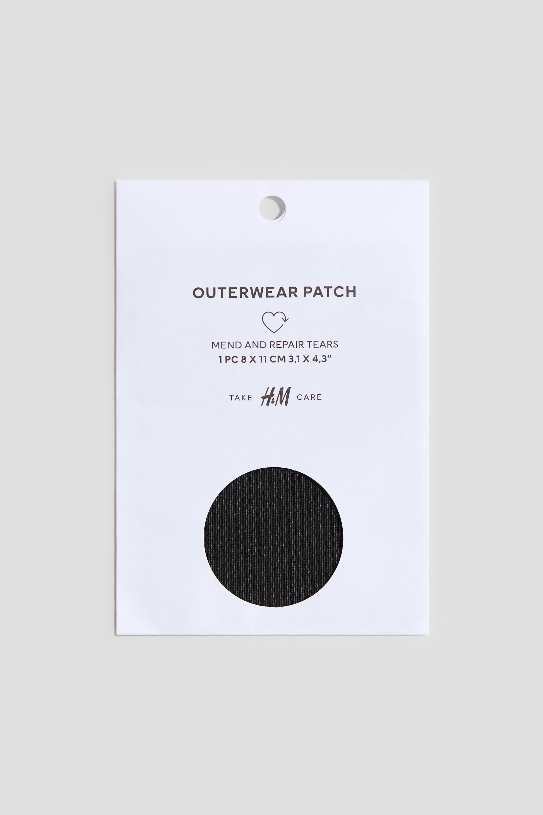 View larger image: The outerwear patch is showcased in front-facing white paper packaging, featuring a circular cutout that reveals a black circular patch with a finely ribbed texture. The packaging also displays product information, a brand logo, and a circular hang hole at the top.