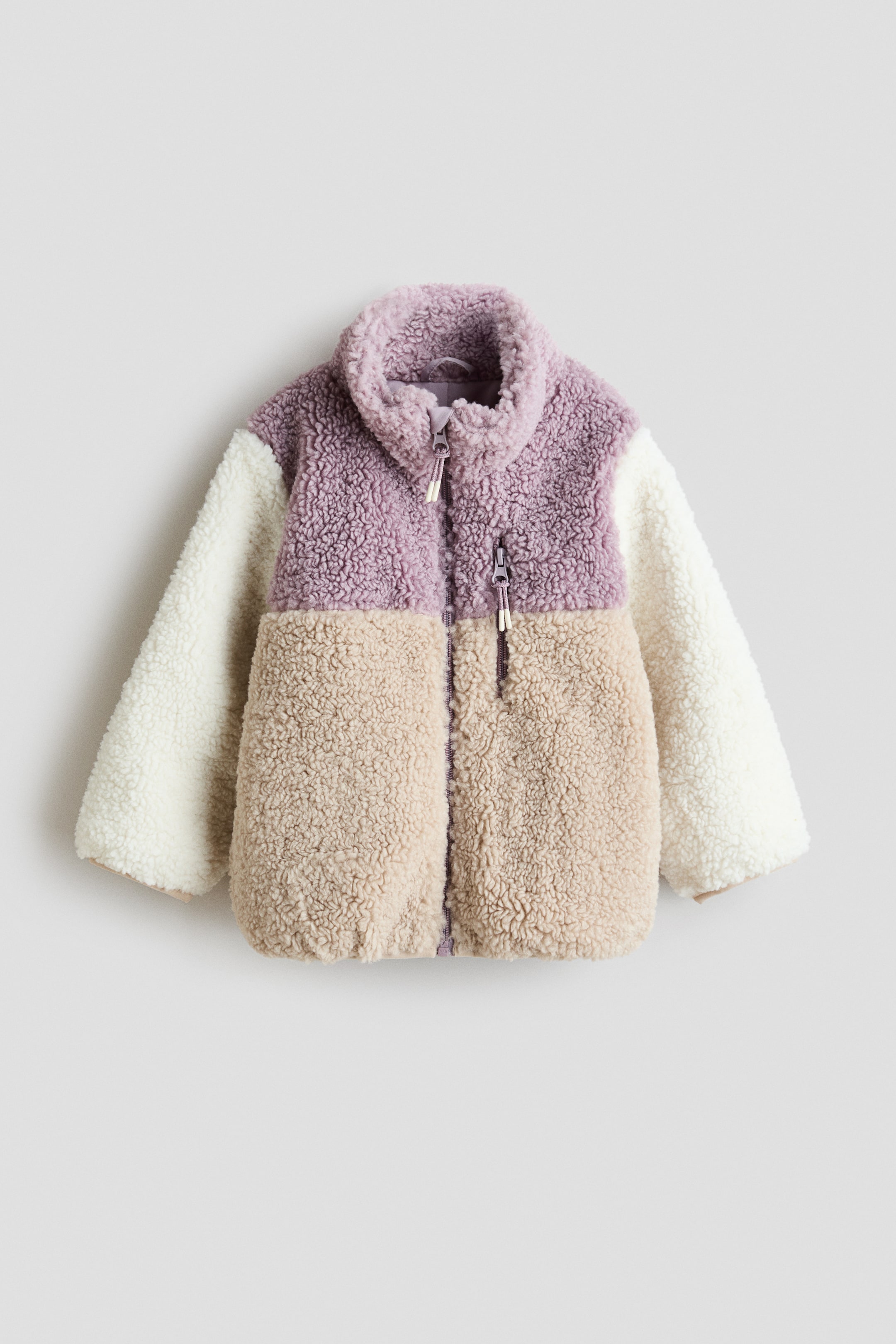 Vis større bilde: En fargeblokkert teddyjakke vises forfra, og har stående krage samt en sentral glidelås med hakebeskytter. Jakken er utformet med lilla overdel, beige underdel og kremfargede ermer, og har en brystlomme med glidelås samt jerseykant ved mansjettene og nederkanten.