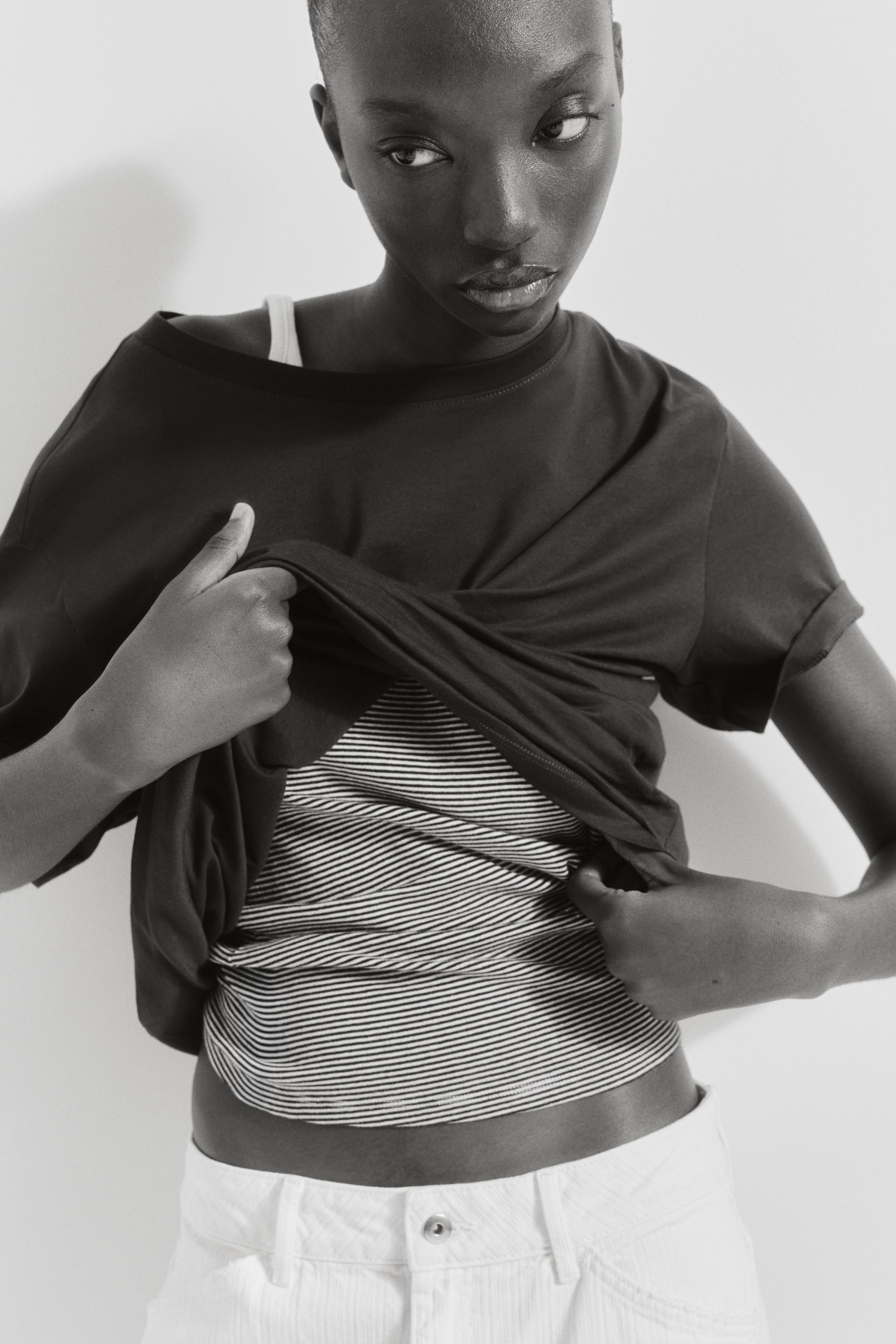 View larger image: A dark t-shirt is being worn with a wide neckline, slightly off the left shoulder, and cuffed short sleeves. The t-shirt is casually draped, partially revealing a striped top underneath.